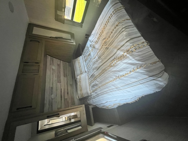 Cozy RV rental bedroom with striped bed, wooden cabinetry, and mirrored dresser. Perfect for your next adventure.. Forest River Palomino Puma 2022