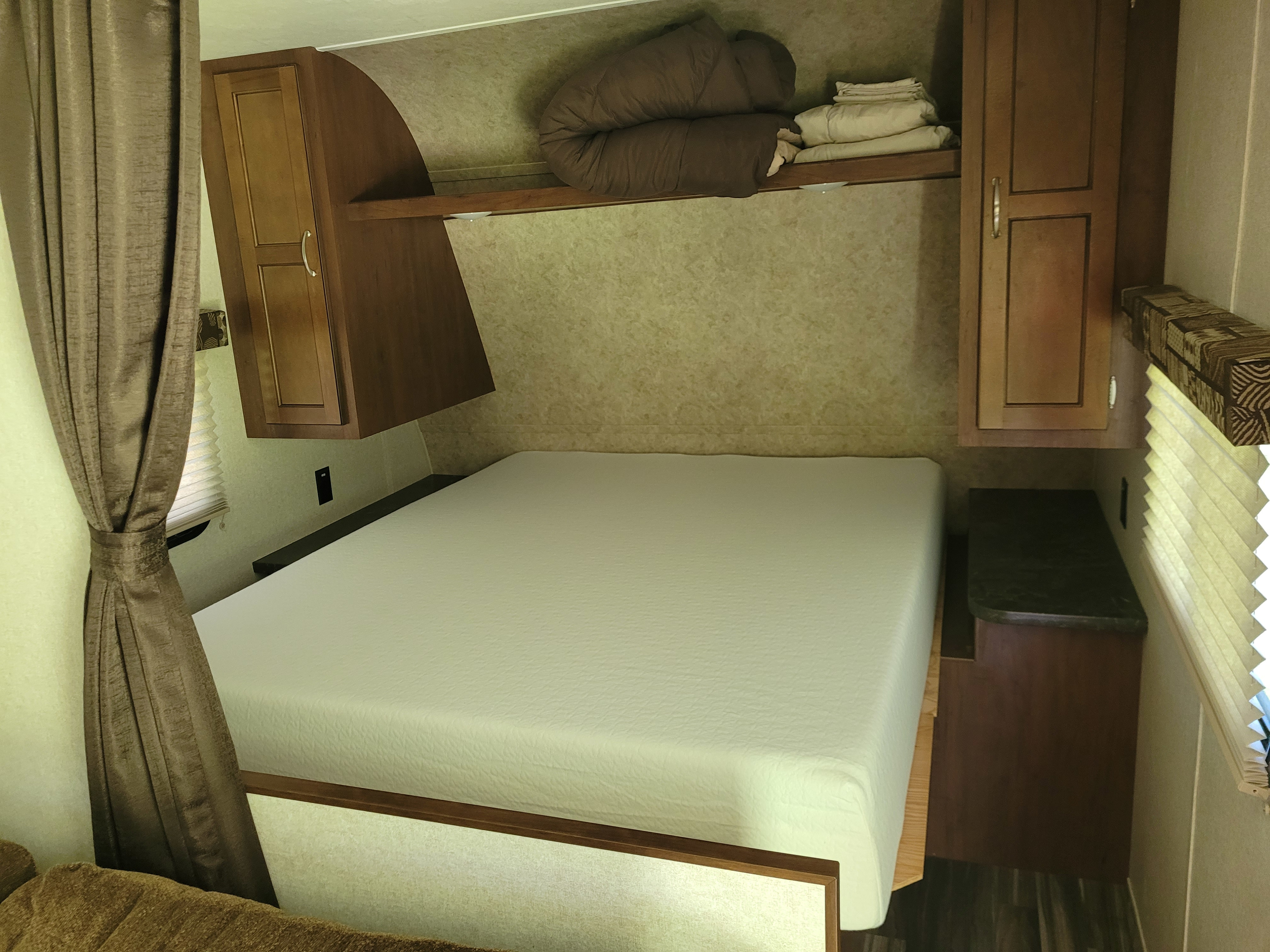 This RV rental bedroom features a clean white bed, overhead storage, and a window with blinds, creating a perfect compact sleeping area.. Jayco Jay Flight SLX 2017