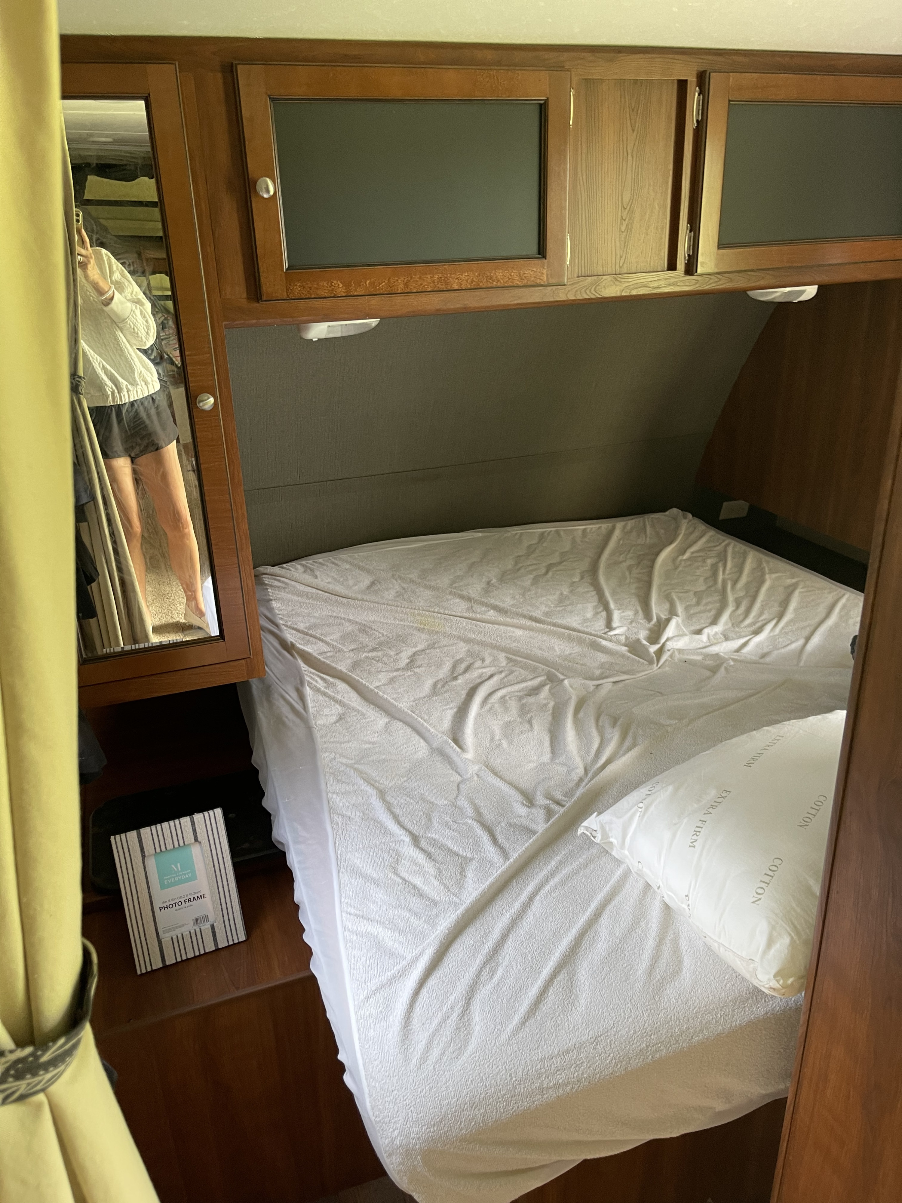 RV rental bedroom: white bed, wood overhead cabinets, and a side mirror reflecting the photographer.. Keystone RV Bullet Ultra Lite 2015
