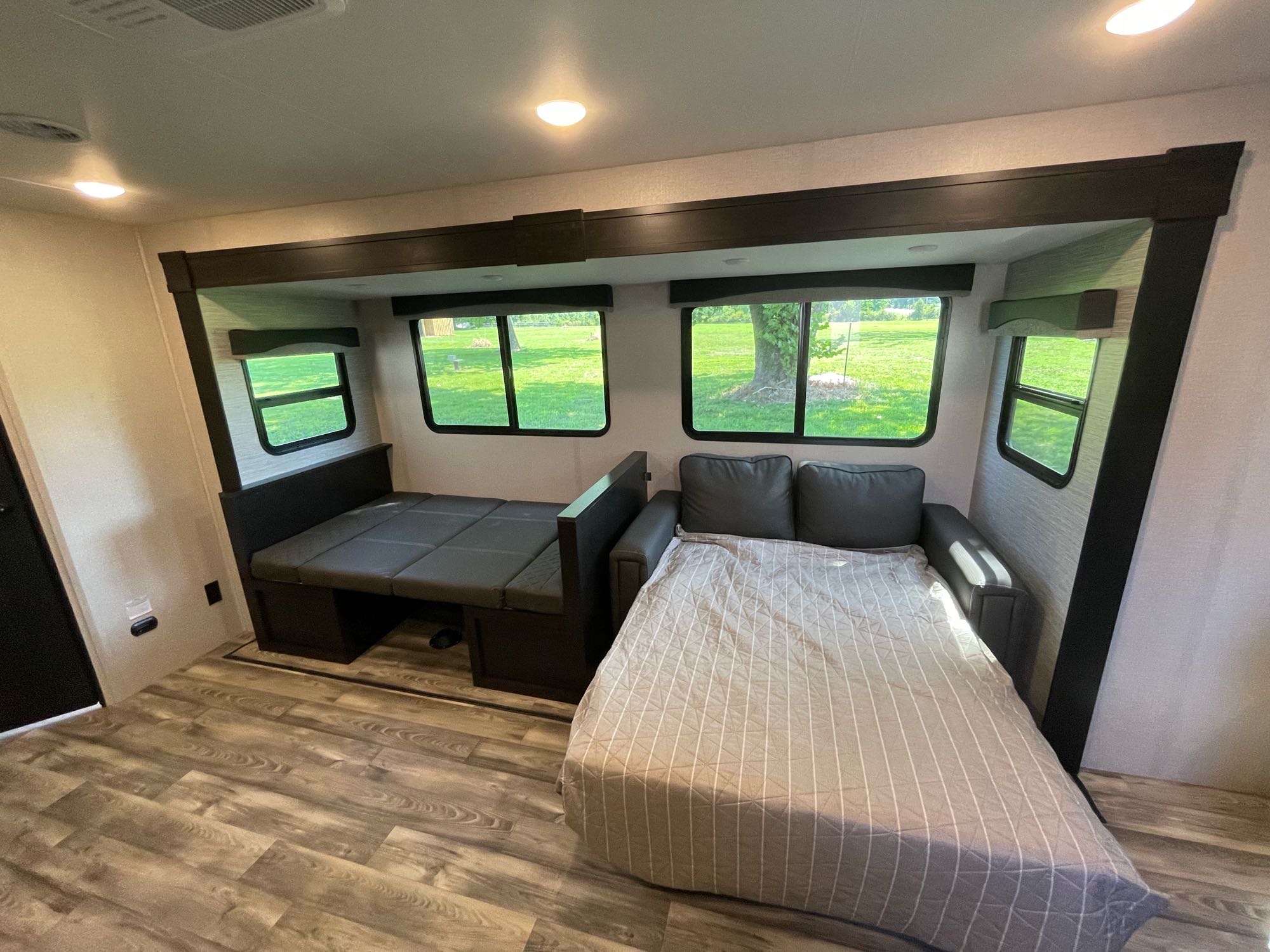RV rental interior with a gray pull-out sofa bed and a convertible dinette bed. Bright windows overlook a green yard.. Starcraft Super Lite 2022