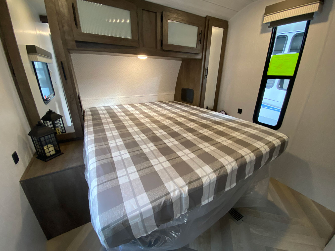 Compact RV rental bedroom: plaid bed, overhead cabinets, and a window. Perfect for road trip adventures.. Forest River Salem 2022