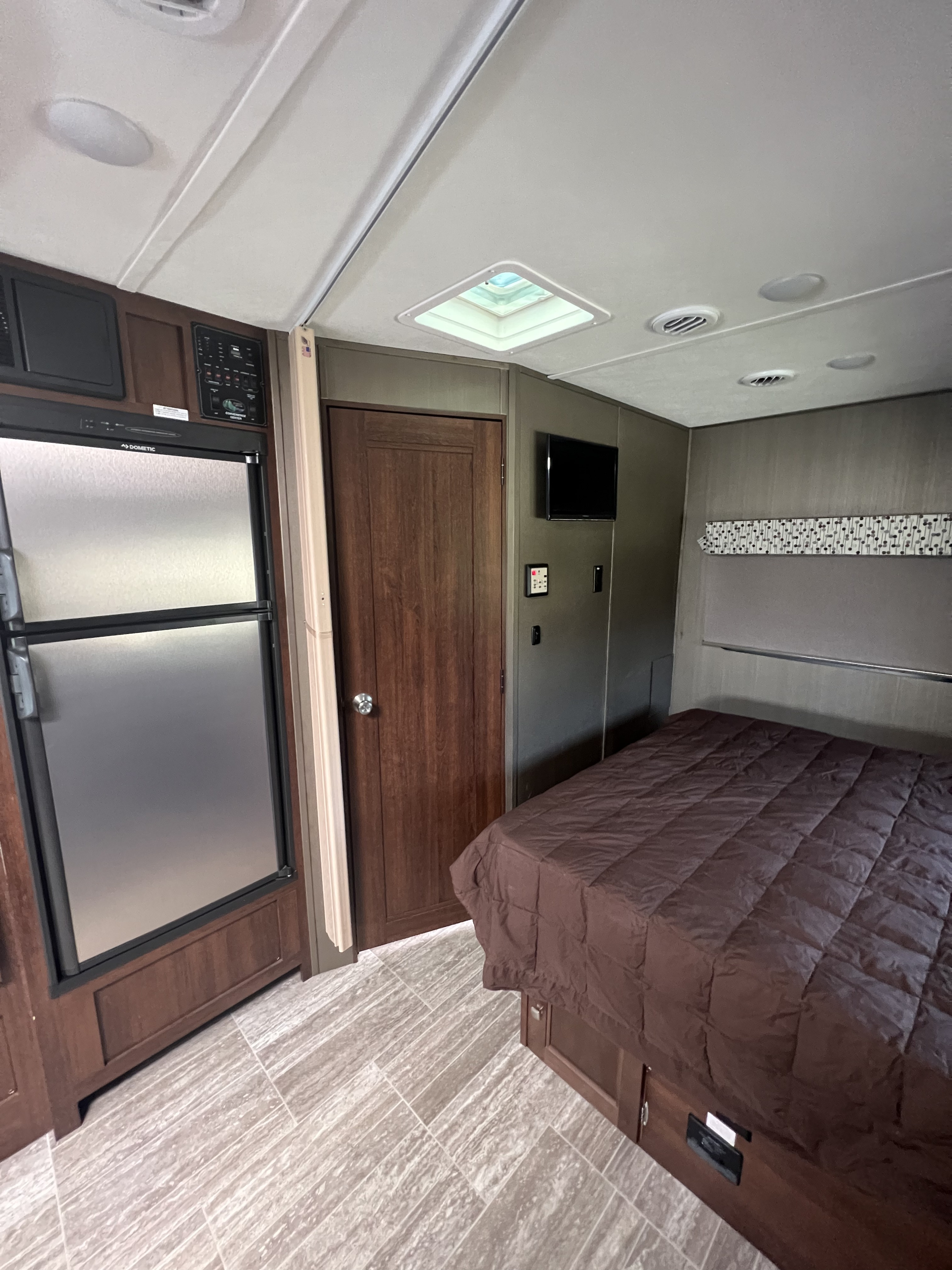 Bright RV rental interior: Bedroom with brown bed & TV; kitchen area features a Dometic fridge and control panel.. Forest River Sunseeker MBS 2019