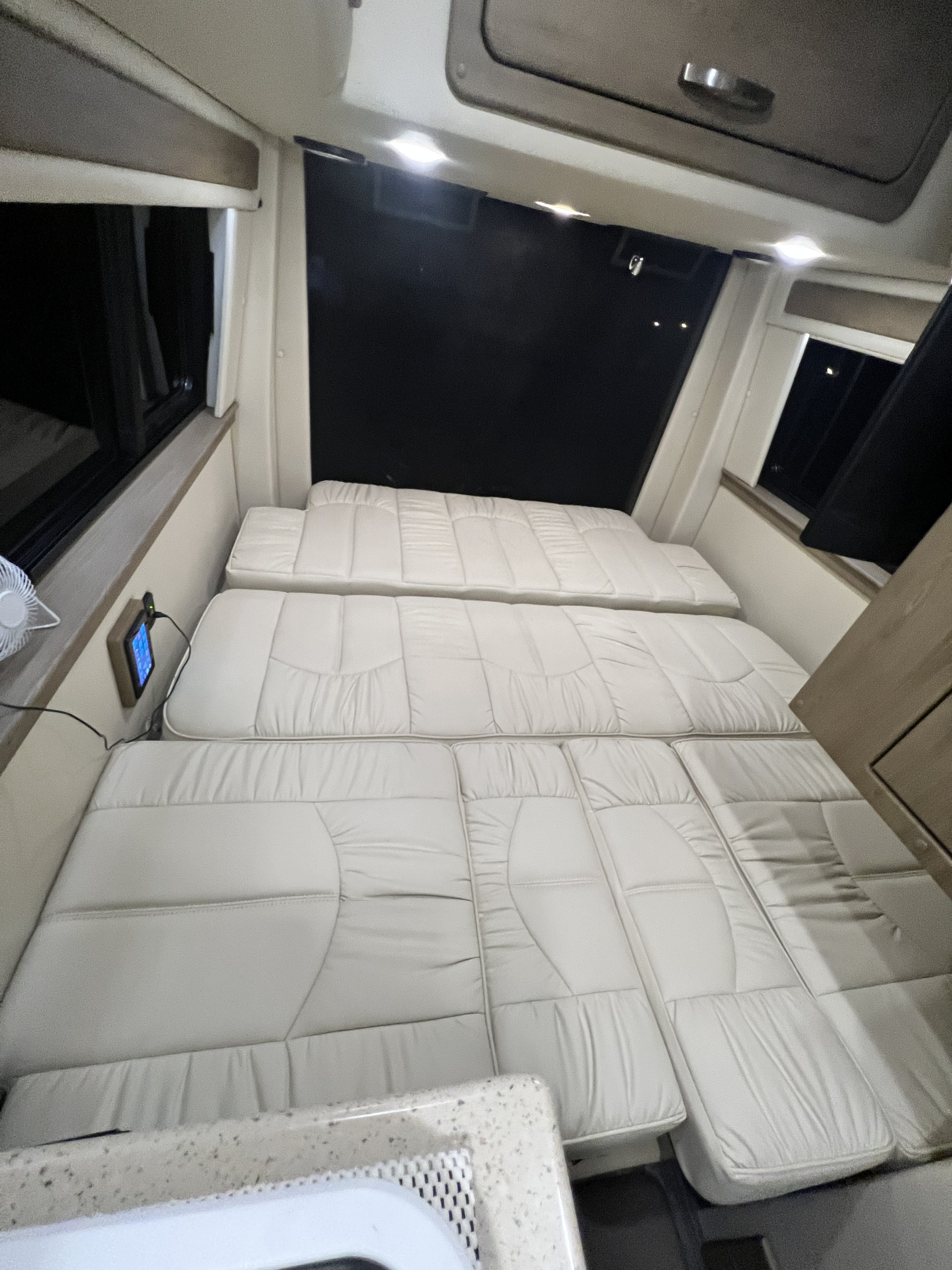 Spacious RV rental interior featuring light-colored cushions arranged as a bed, with windows & control panel access.. Midwest Automotive Designs Midwest Automotive Designs Class B 2021