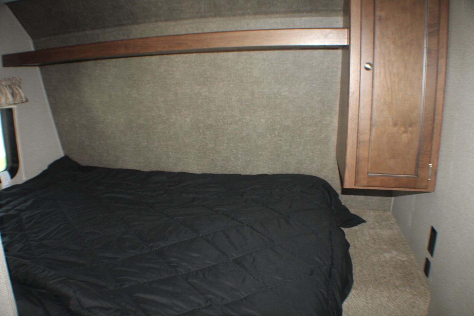 Cozy RV rental bedroom features a comfy black bed, overhead shelf, and wall-mounted cabinet, perfect for your travels.. Keystone RV Hideout LHS Mini 2018