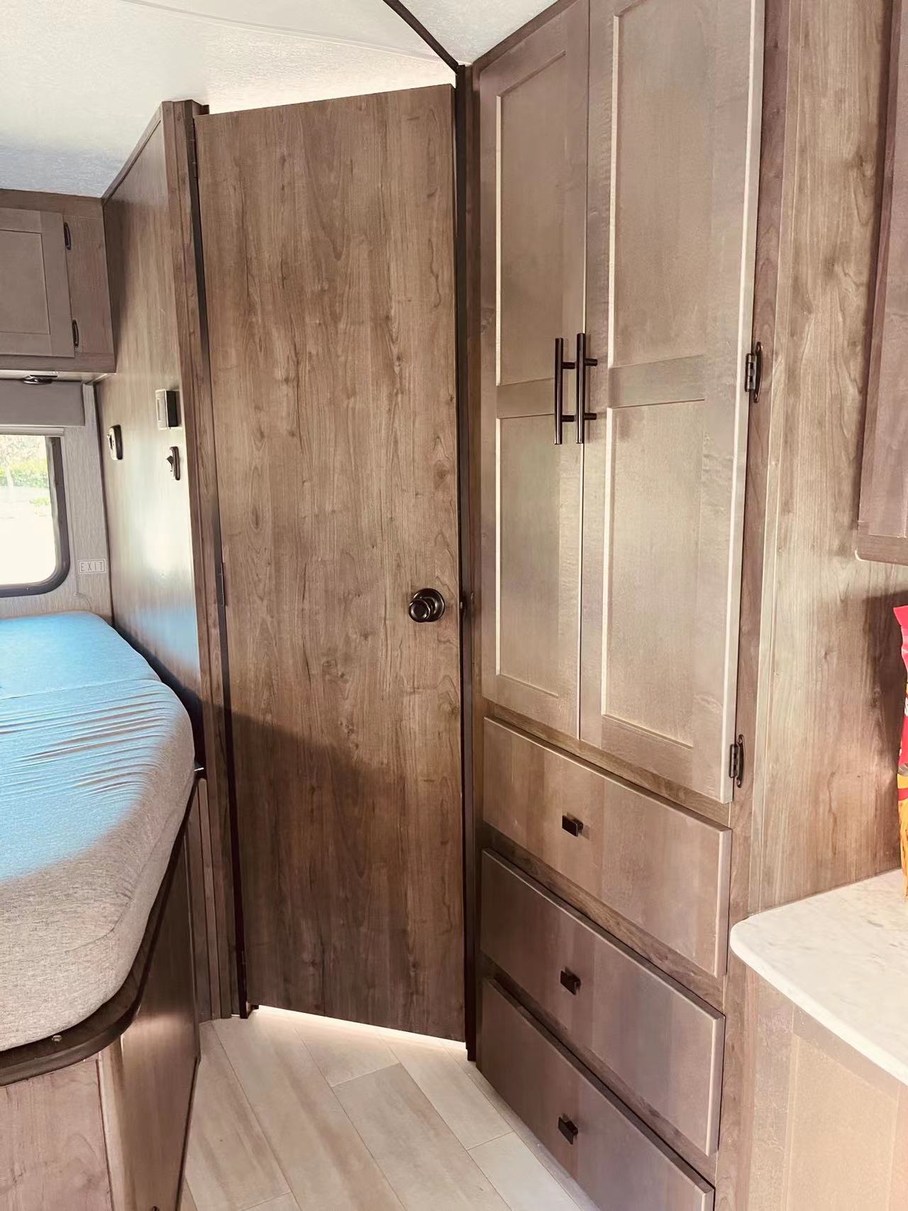 RV rental: Bright RV bedroom showing a light bed, a wooden door, and wood-grain storage cabinets with drawers.. Forest River Coachmen Leprechaun 2022