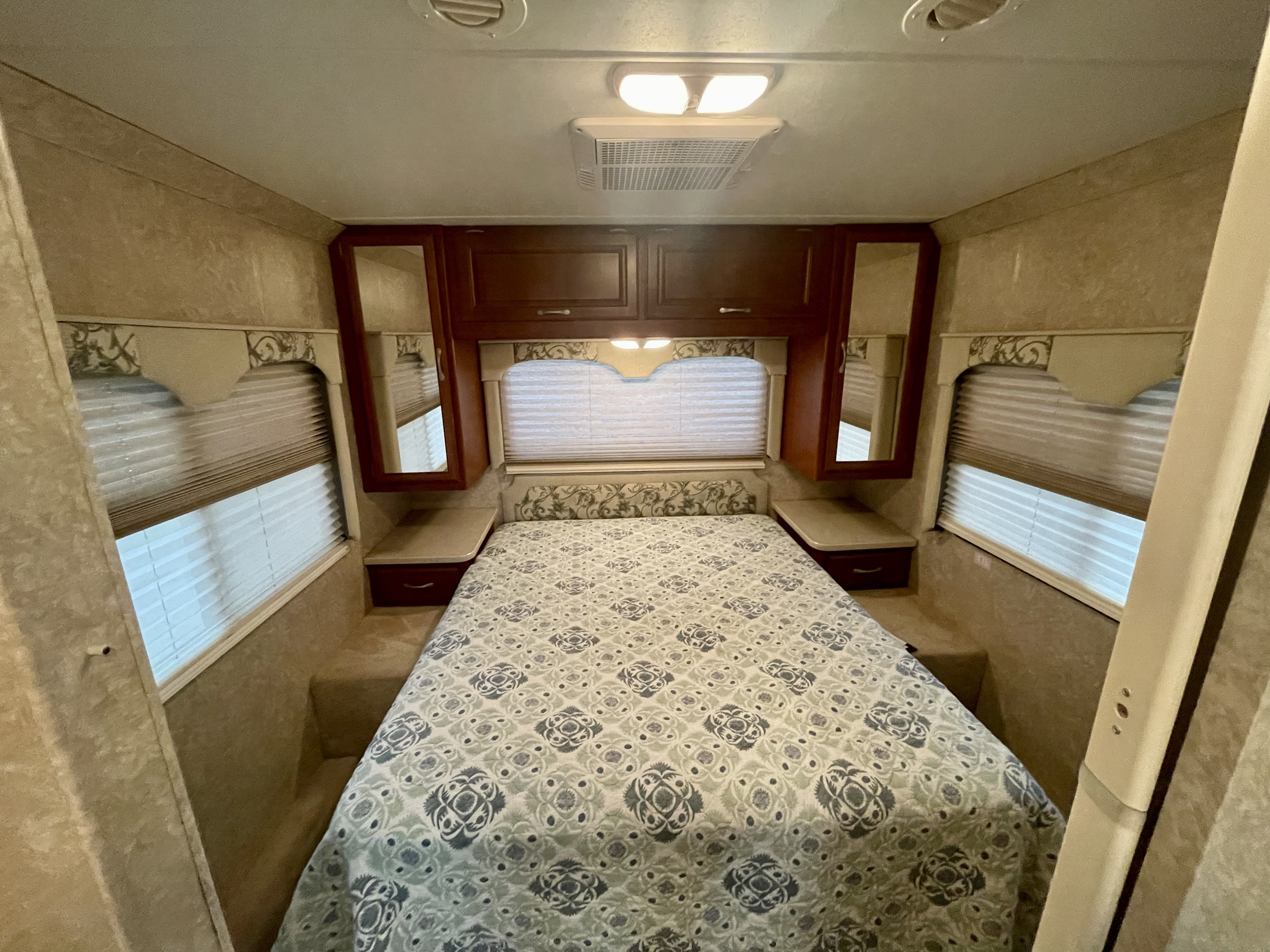 RV rental bedroom with patterned bed, overhead cabinets, and windows. This compact space offers comfortable accommodations.. Four Winds Hurricane 2007