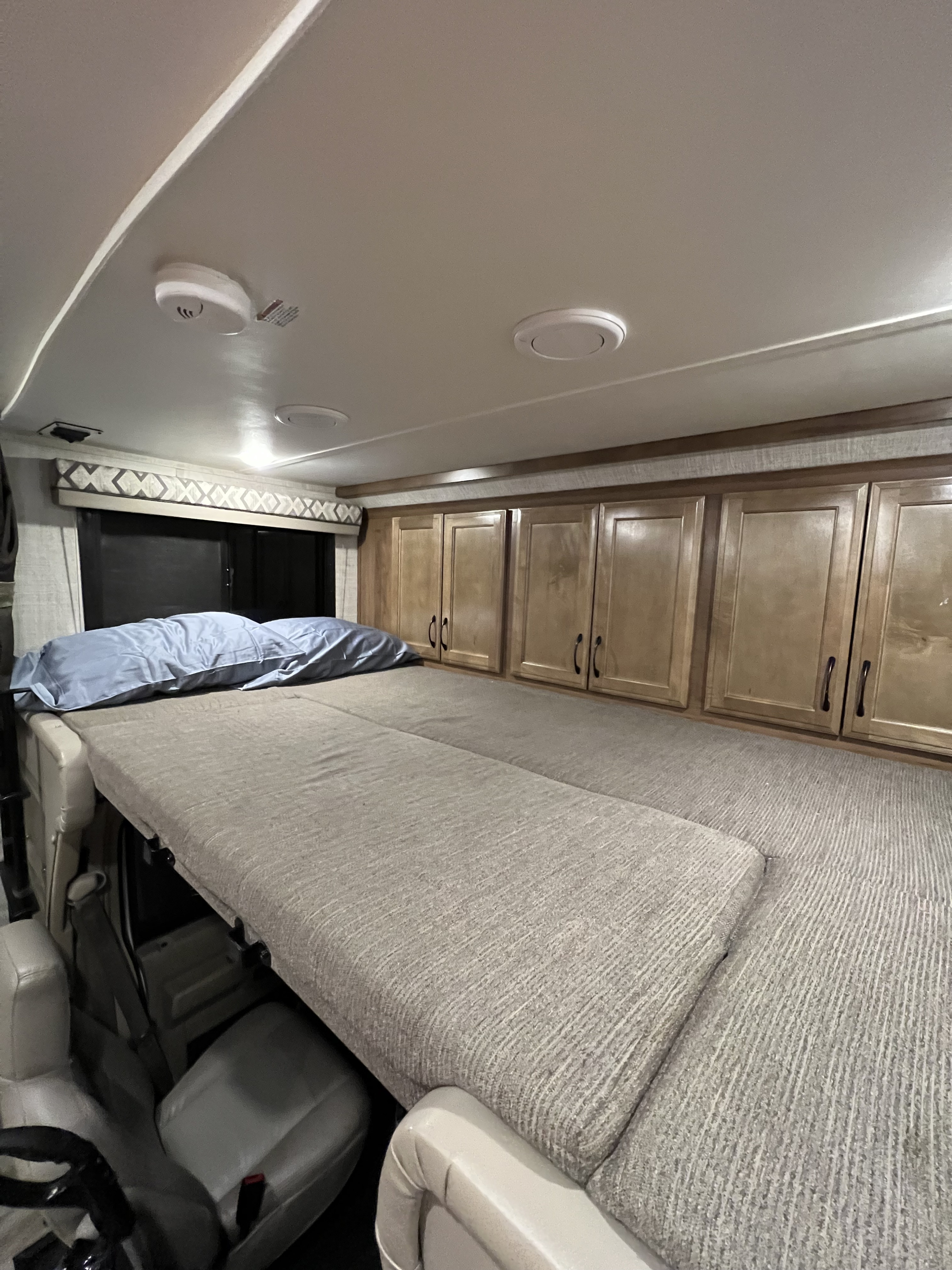 Inside an RV rental, a cozy cab-over bunk bed with a blue pillow and overhead storage offers comfortable sleeping space.. Gulf Stream Conquest 2020