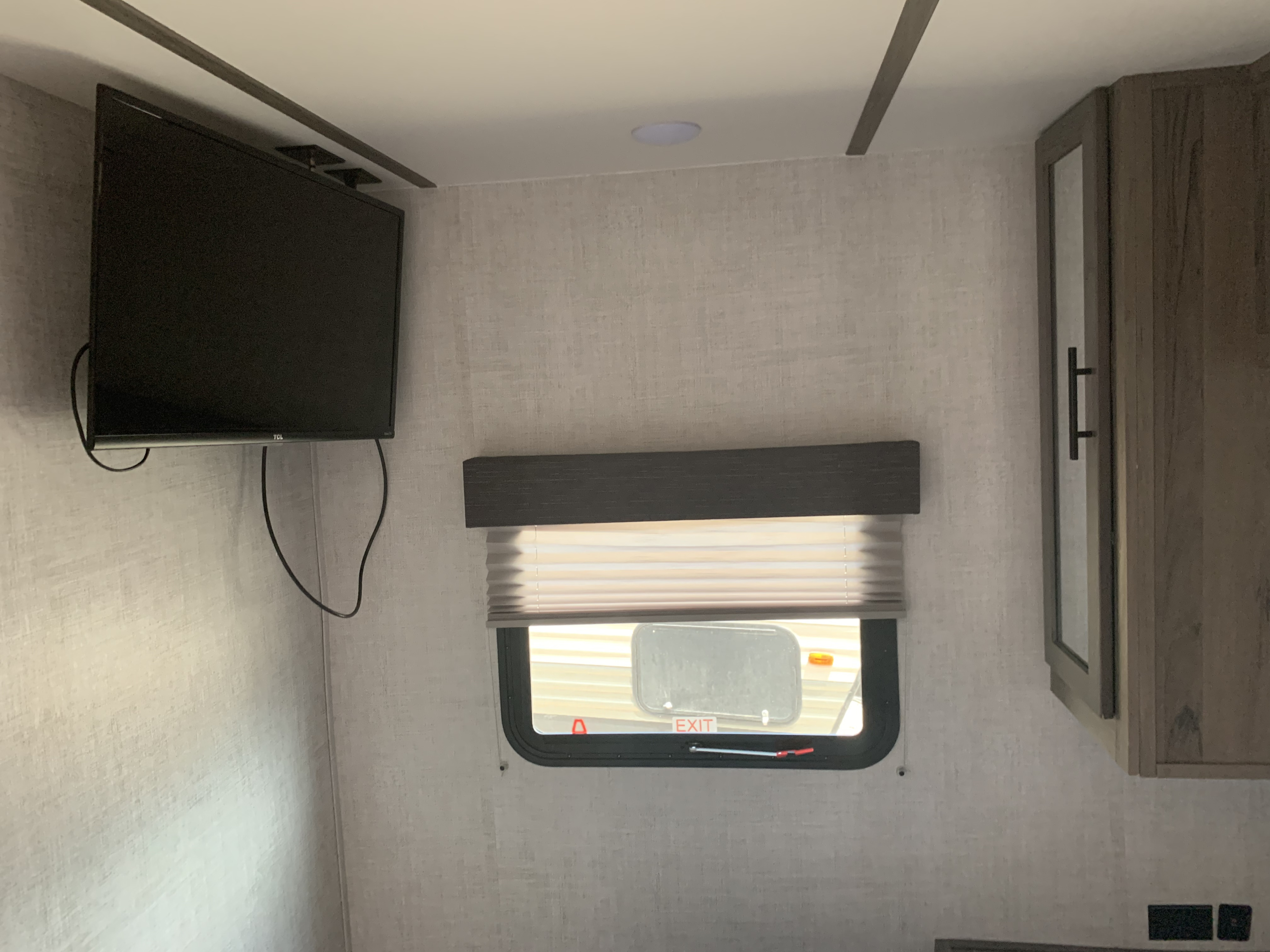 An RV rental interior with a wall-mounted TV, window featuring white pleated blinds, and wooden cabinet.. Gulf Stream Conquest LE 2021