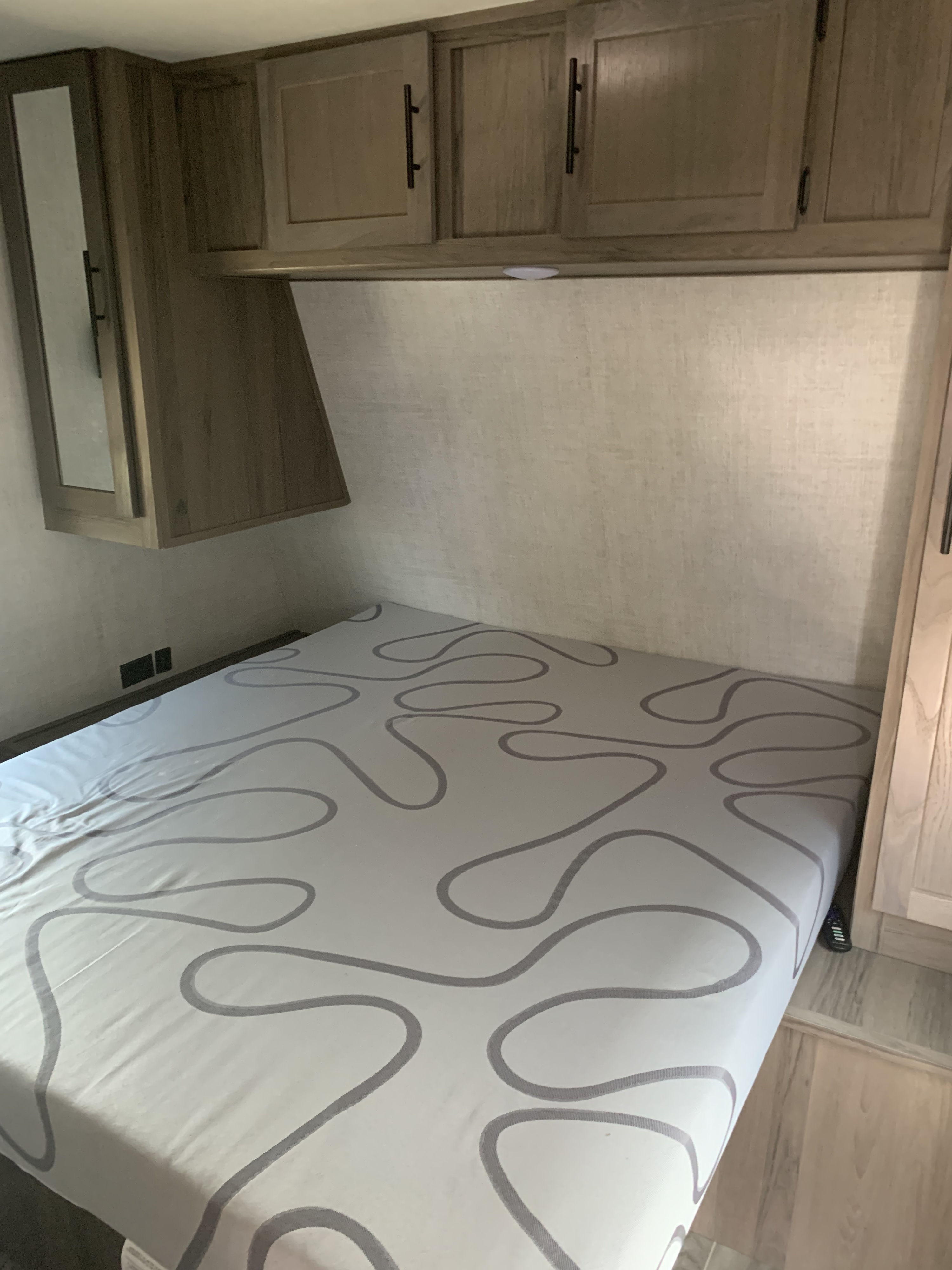 An RV rental bedroom offers a cozy space with a bed, distinctive patterned sheets, overhead cabinets, and a mirror on the left wall.. Gulf Stream Conquest LE 2021