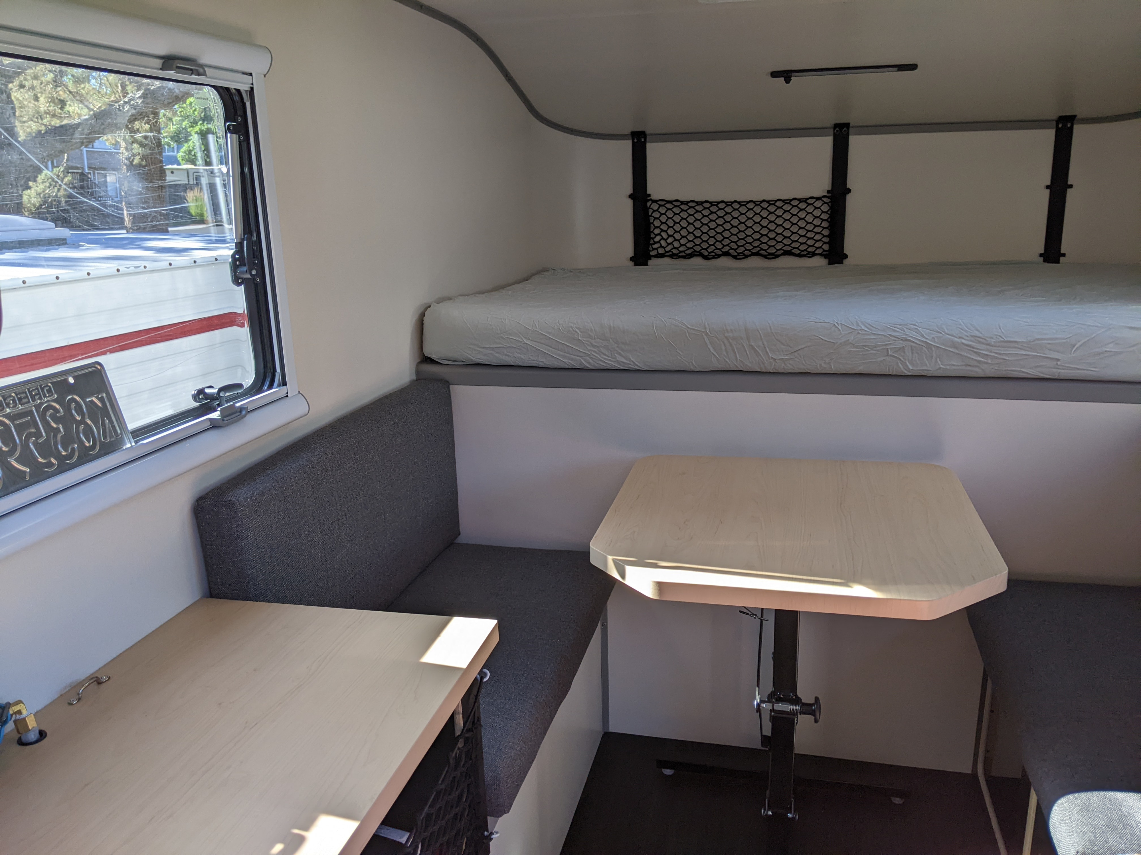 Compact RV rental interior: features a bunk bed over a dinette with a light wood table and grey benches.. Adventurer SCOUT Olympic 2022
