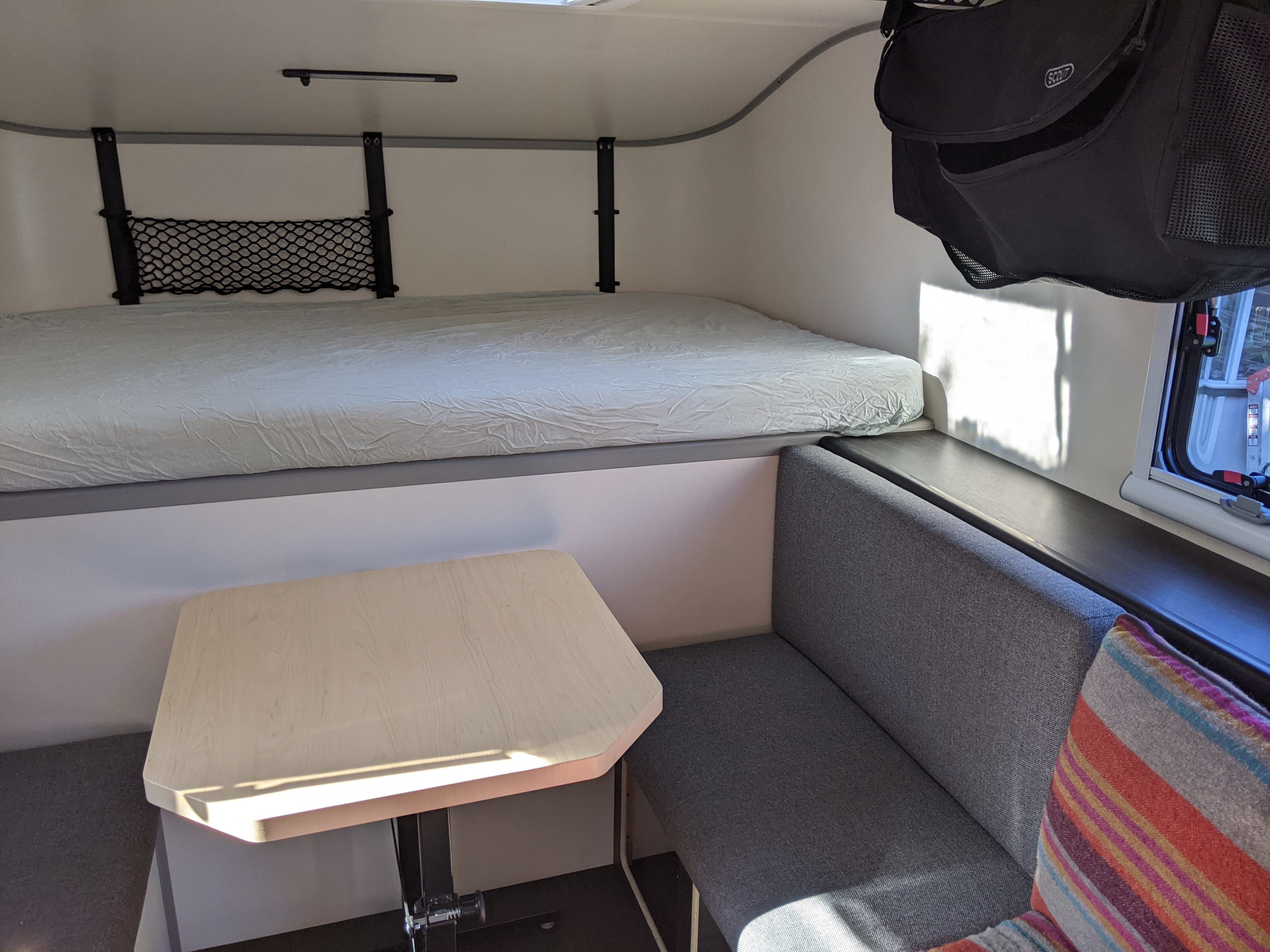 Inside a modern RV rental: comfortable dinette and elevated bed with clever storage solutions for road trip adventures.. Adventurer SCOUT Olympic 2022