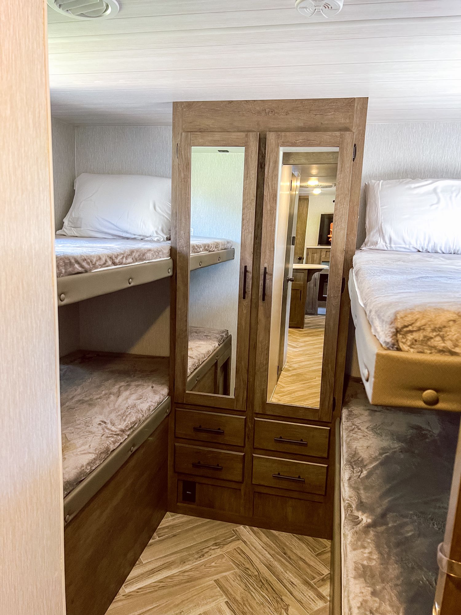 Inside an RV rental: view of bunk beds on left and right, flanking a mirrored storage cabinet. Wood-look floor.. Forest River Wildwood X-Lite 2022