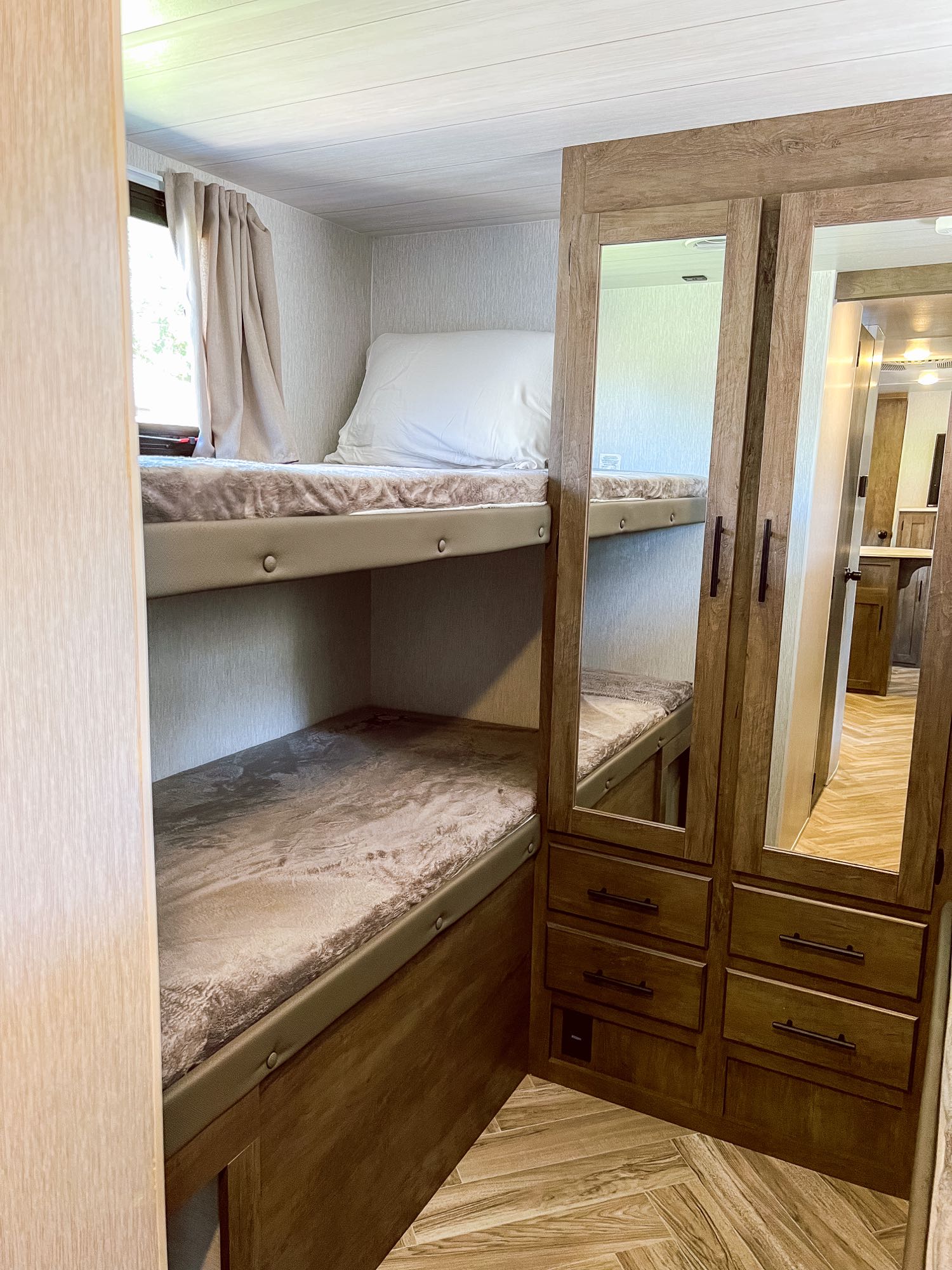 Cozy RV rental interior featuring bunk beds with a window and a mirrored wardrobe with drawers for convenient storage.. Forest River Wildwood X-Lite 2022