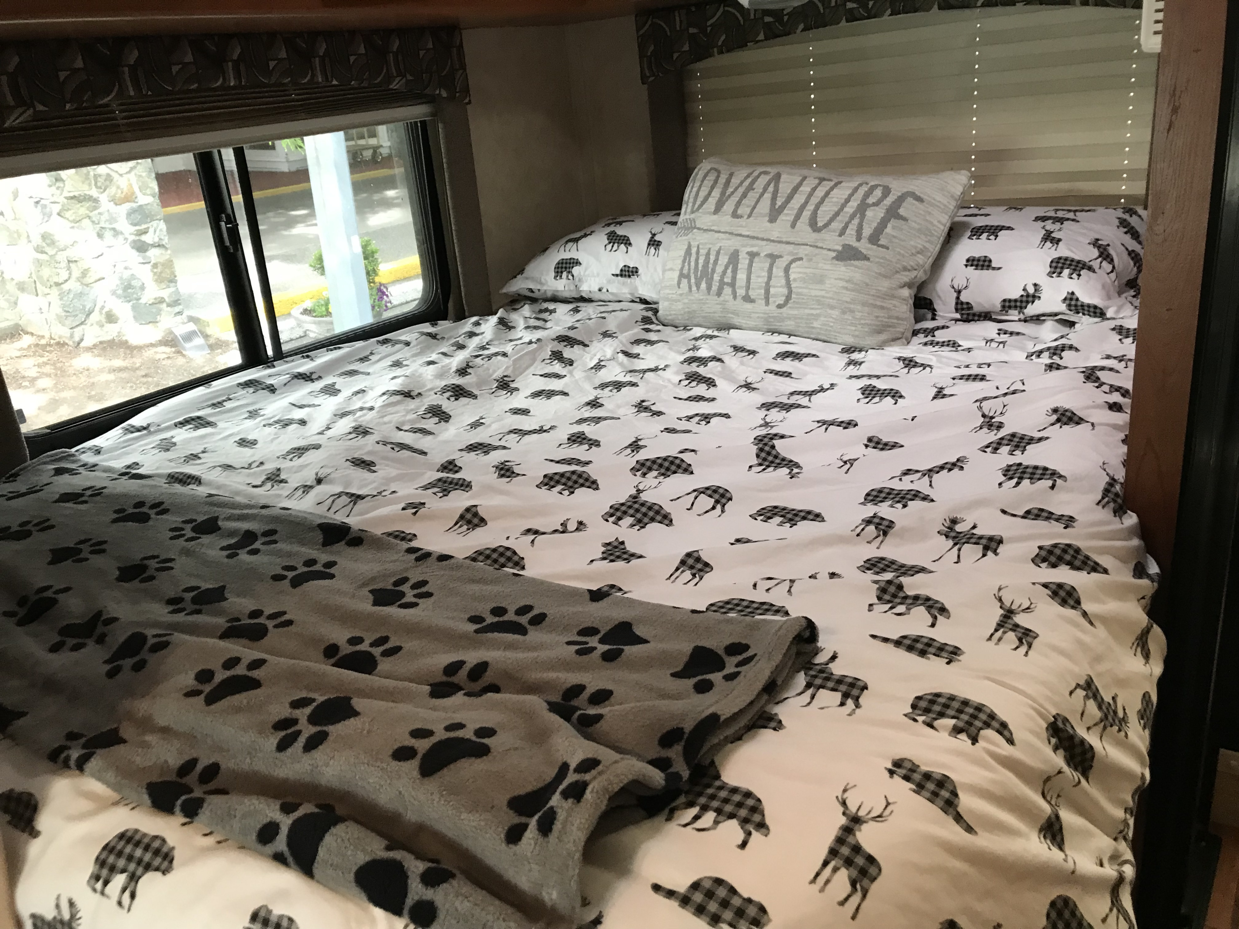 Cozy RV bed with "Adventure Awaits" pillow, plaid animal bedding, and paw print blanket, ideal for your RV rental.. Ford Coachmen Freelander 2011