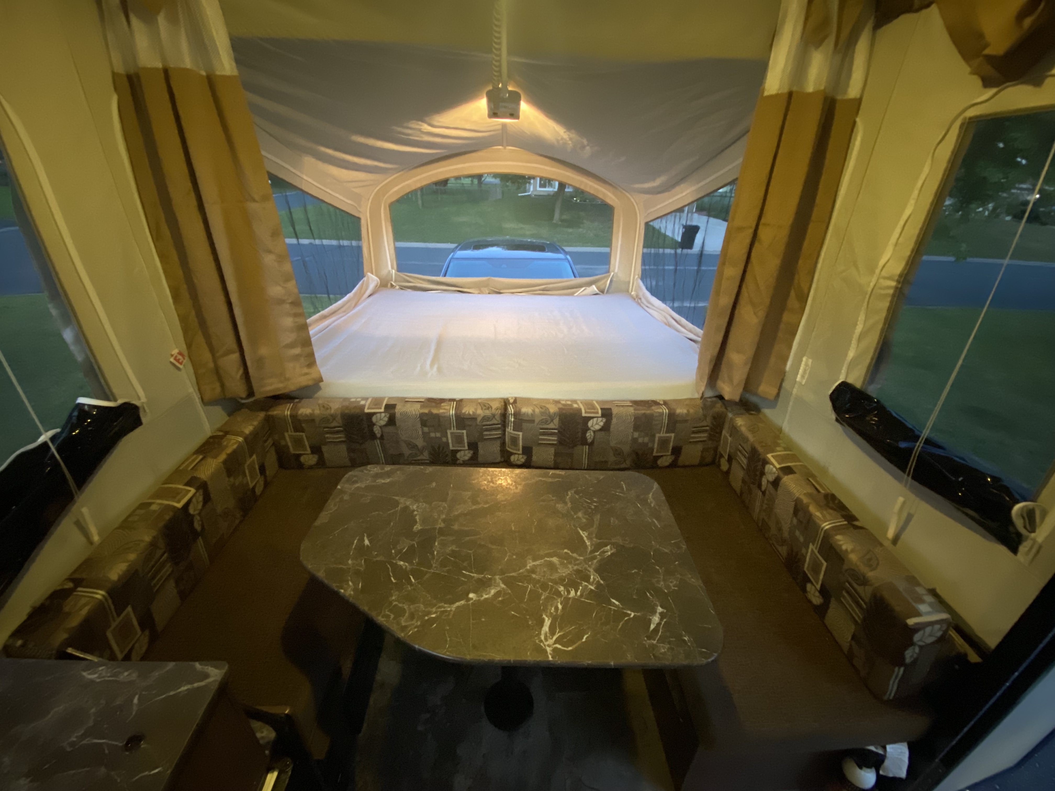 Cozy RV rental pop-up camper interior, showcasing a large bed, patterned dinette, and bright windows overlooking outside.. Jayco Jay 2016