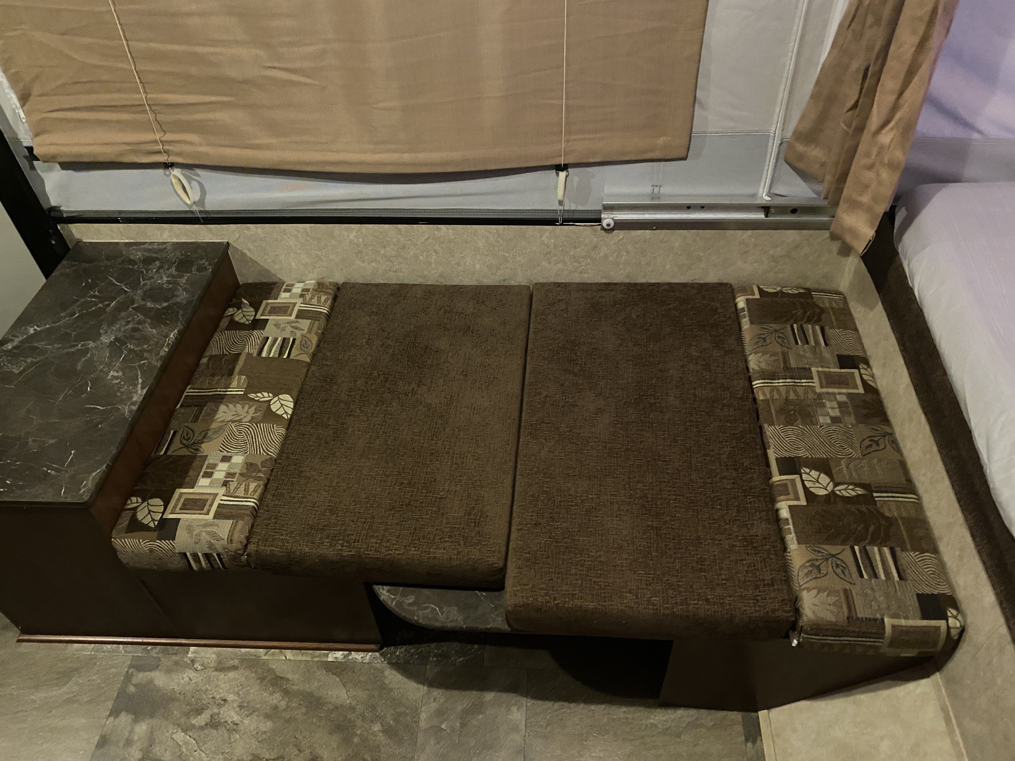 RV rental interior: bench seating with patterned cushions, a small table to the left, and a bed on the right.. Jayco Jay 2016