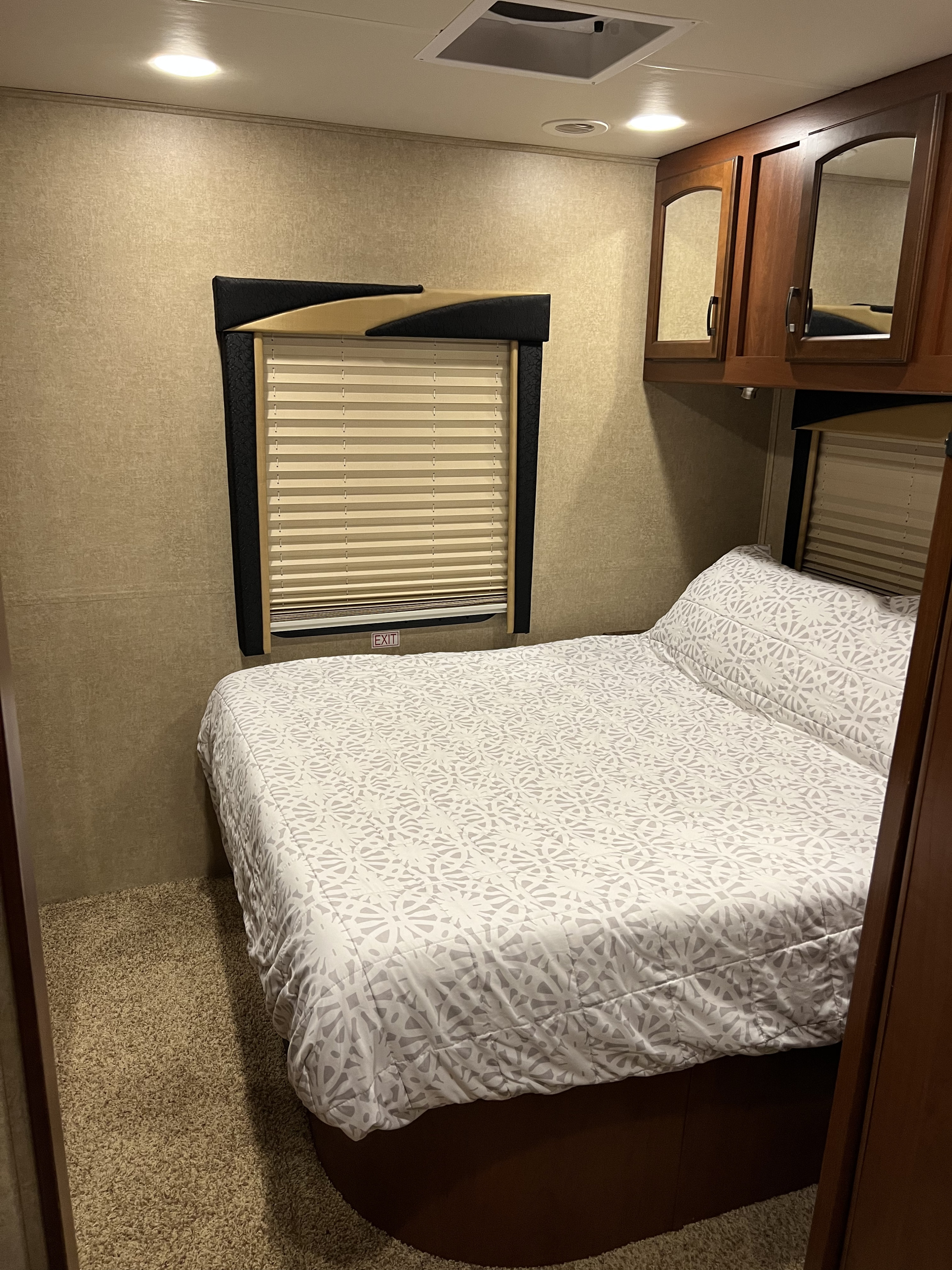 Cozy RV rental bedroom with a patterned bed, window (with 'EXIT' sign), and mirrored overhead cabinets.. Jayco Greyhawk 2015