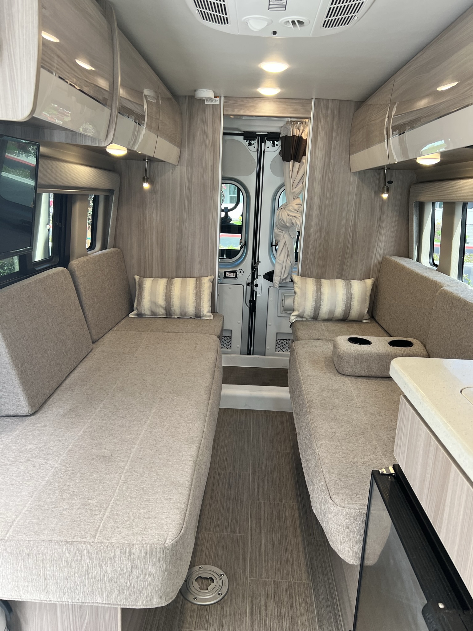 Modern rv rental interior: A narrow view of twin upholstered bench seats facing each other, overhead cabinets & galley.. Thor Sequence 2023