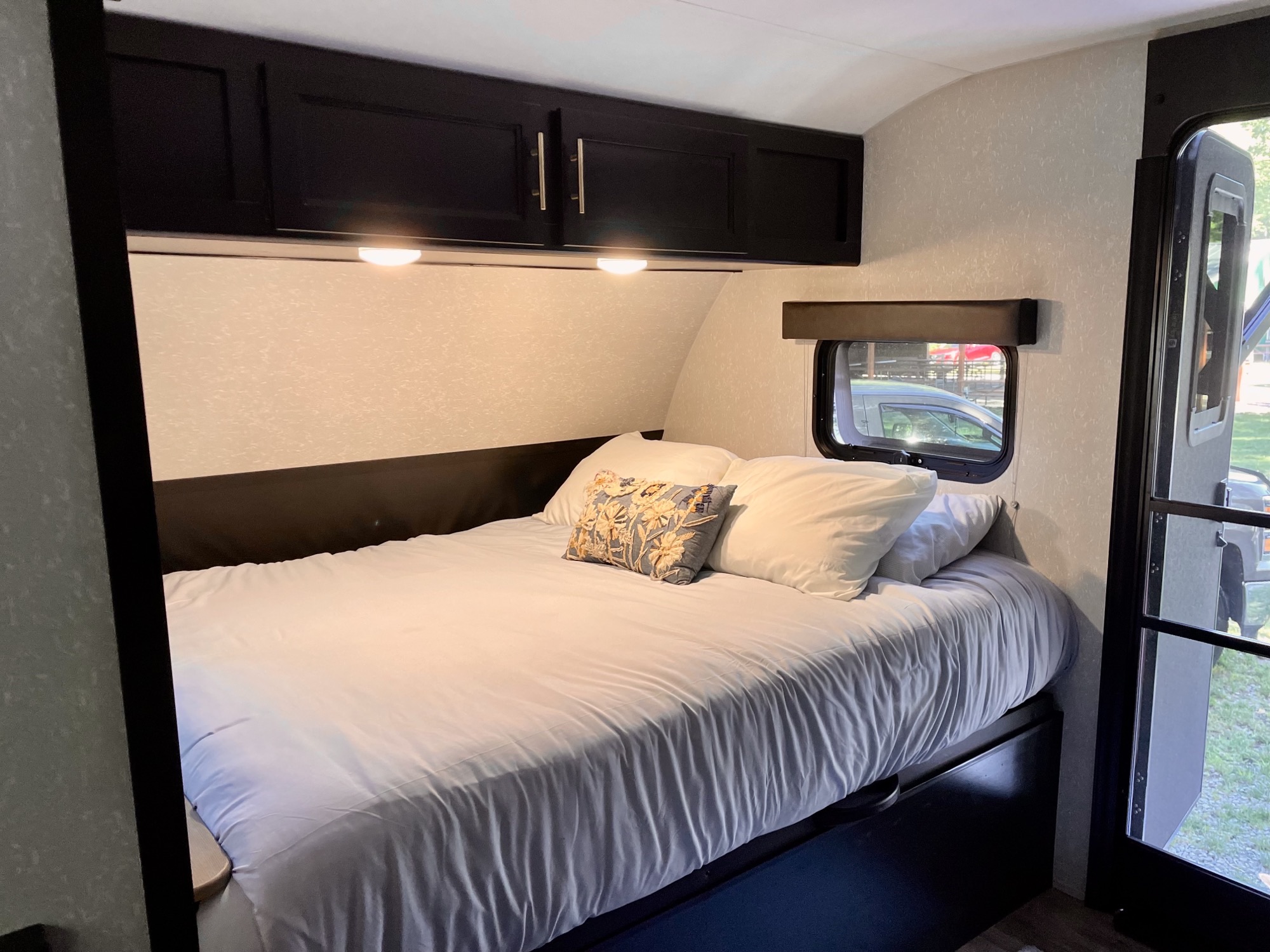 Cozy RV rental bedroom with a comfy bed, overhead cabinets, and window views. Perfect camper interior.. Forest River Cherokee Wolf Pup Black Label 2021