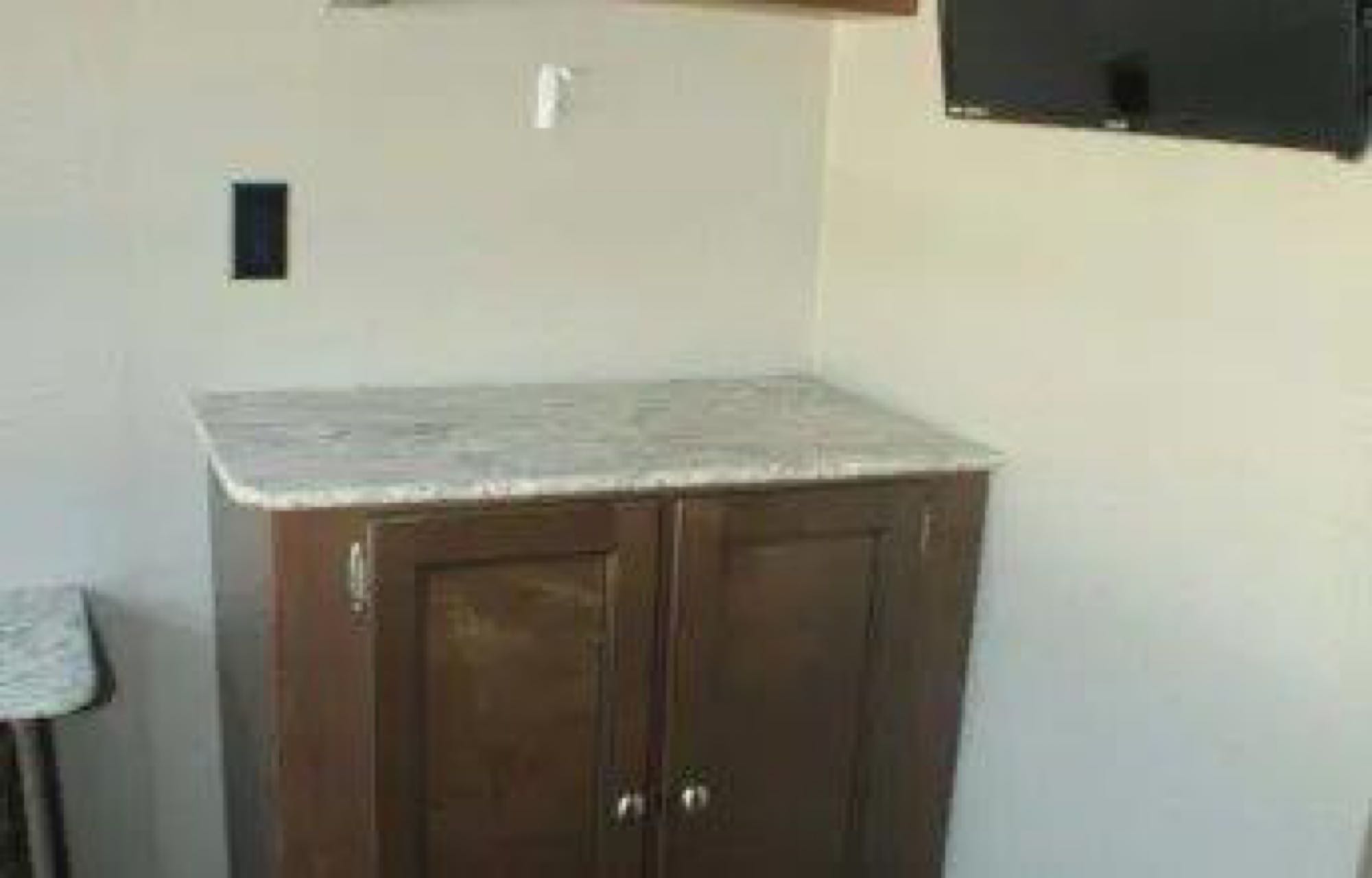 RV rental interior: practical space with a dark wood cabinet, light counter, wall outlet, and mounted TV.. Keystone RV Hideout LHS Mini 2018