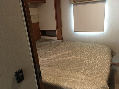 Inside an RV rental: a practical bedroom with a neatly made bed, window shade, and built-in cabinetry.. Winnebago Vista 2017
