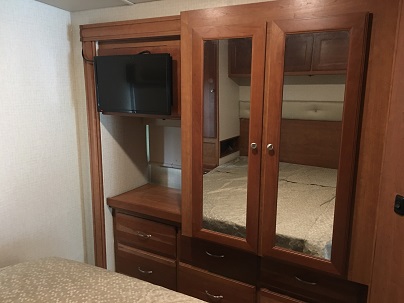 RV rental bedroom: Mirrored wardrobe reflects the bed, next to a wall-mounted TV above a wood dresser.. Winnebago Vista 2017