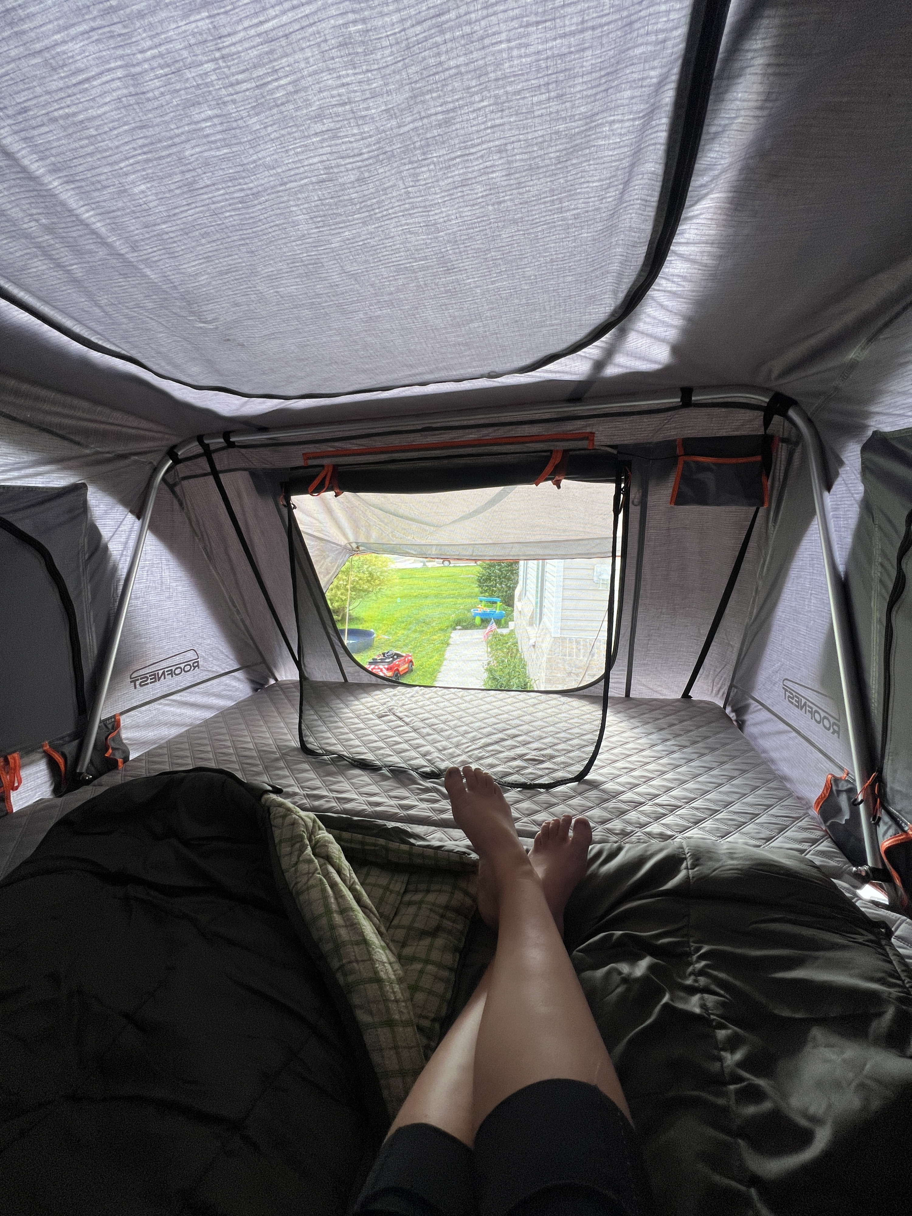 Comfortable camping in a Roofnest rooftop tent, feet propped. An RV rental option with a homey backyard view.. Land Rover Range Rover Sport 2006