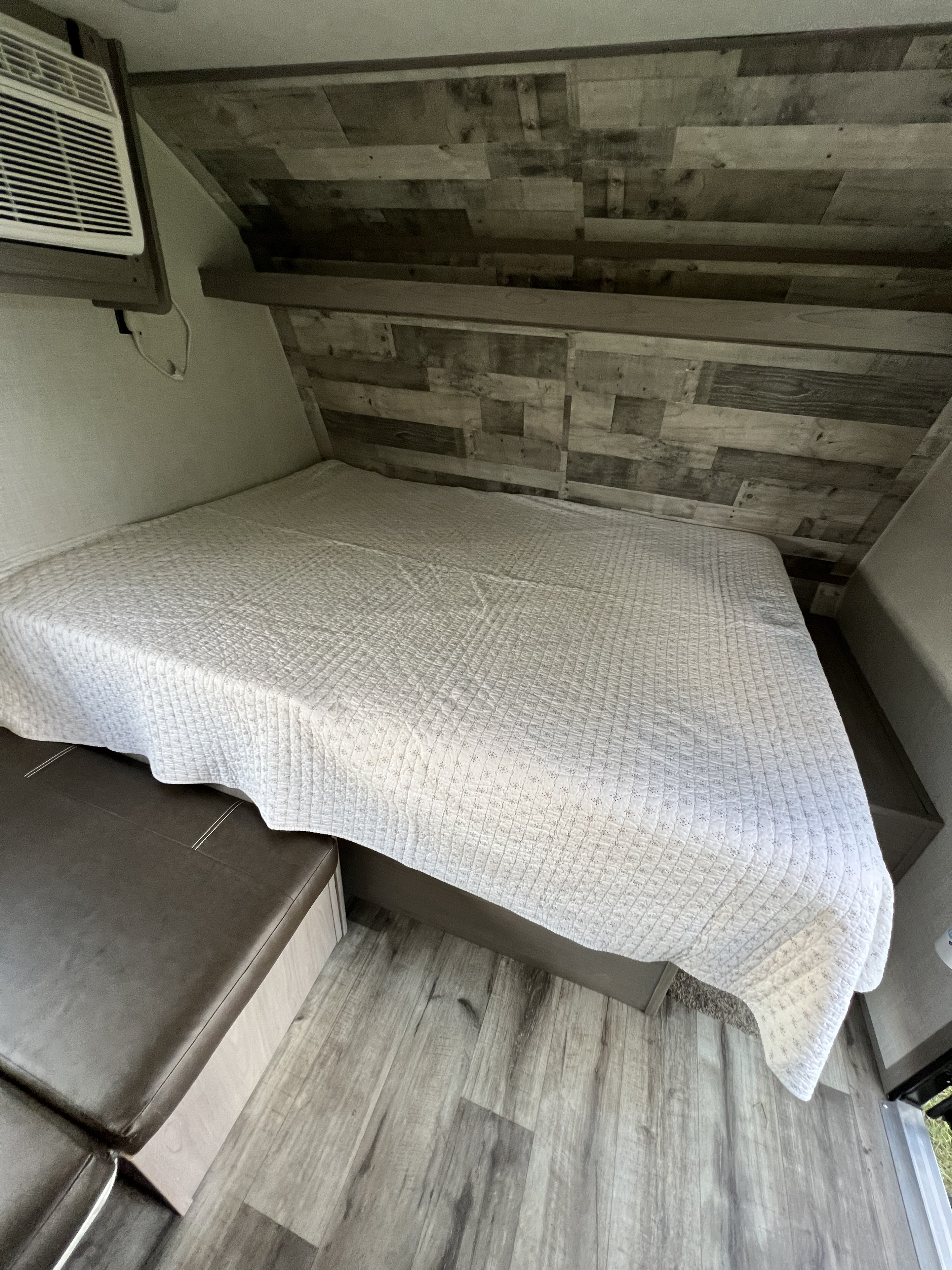 Cozy RV rental bedroom with a quilted bedspread, wood-paneled wall, and AC unit for comfortable camper stays.. Dutchmen Coleman Lantern LT 2022