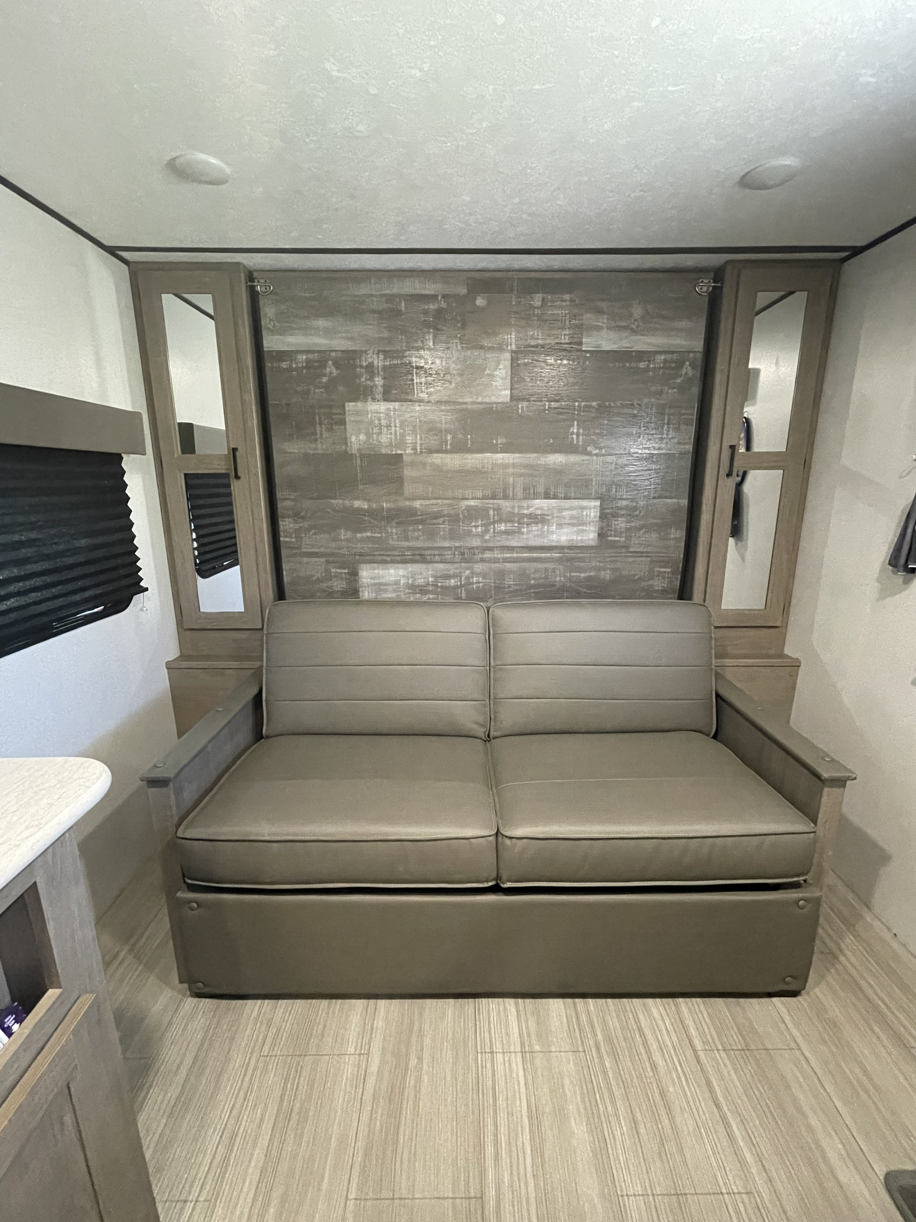 Modern RV rental interior with a gray sofa, wood-paneled wall, and mirrored storage cabinets.. Keystone Travel trailer Hideout 2021