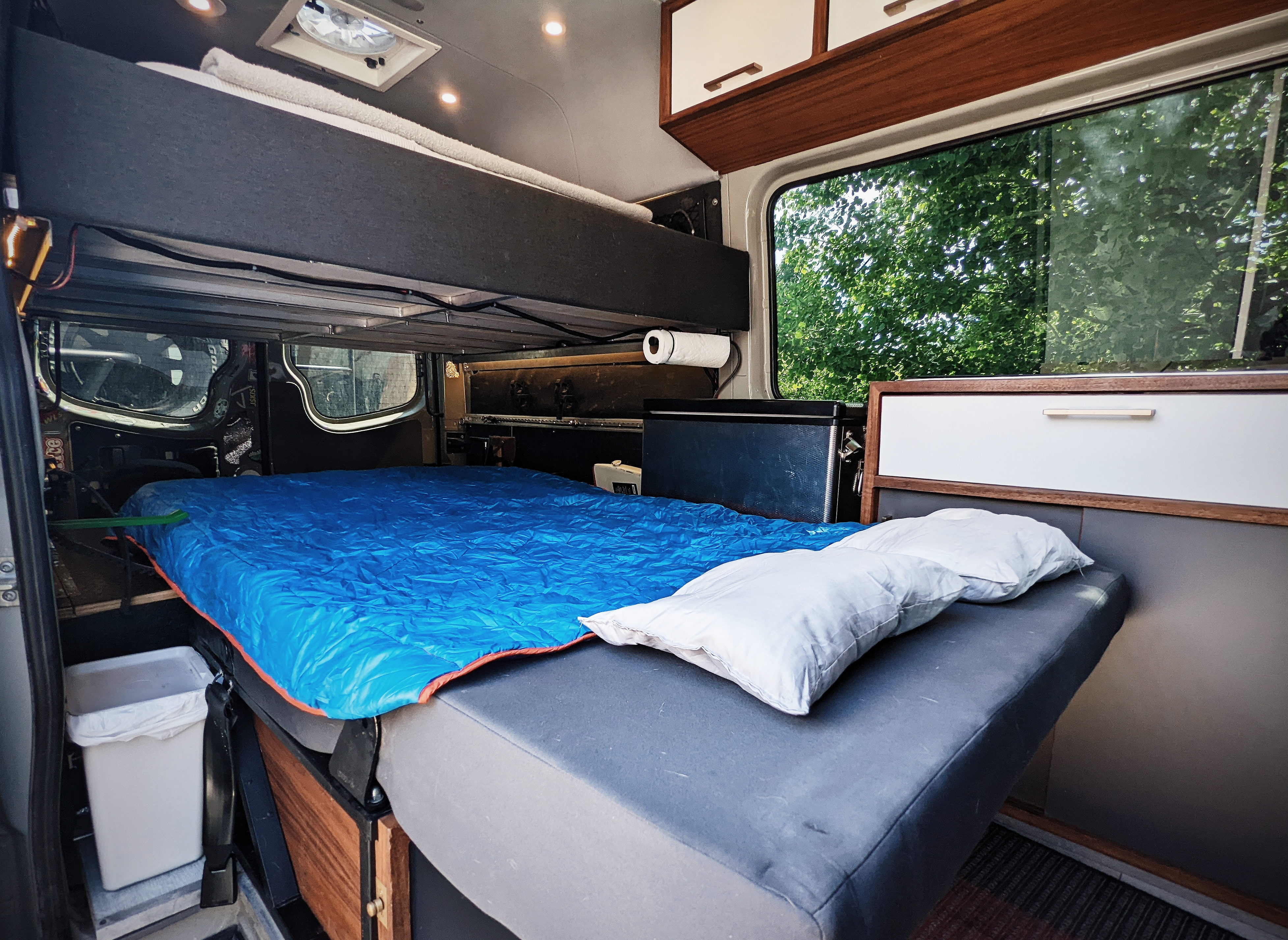 This RV rental offers a spacious interior: main bed with blue sleeping bag, an upper bunk, and ample storage.. Mercedes-Benz Sprinter 2017