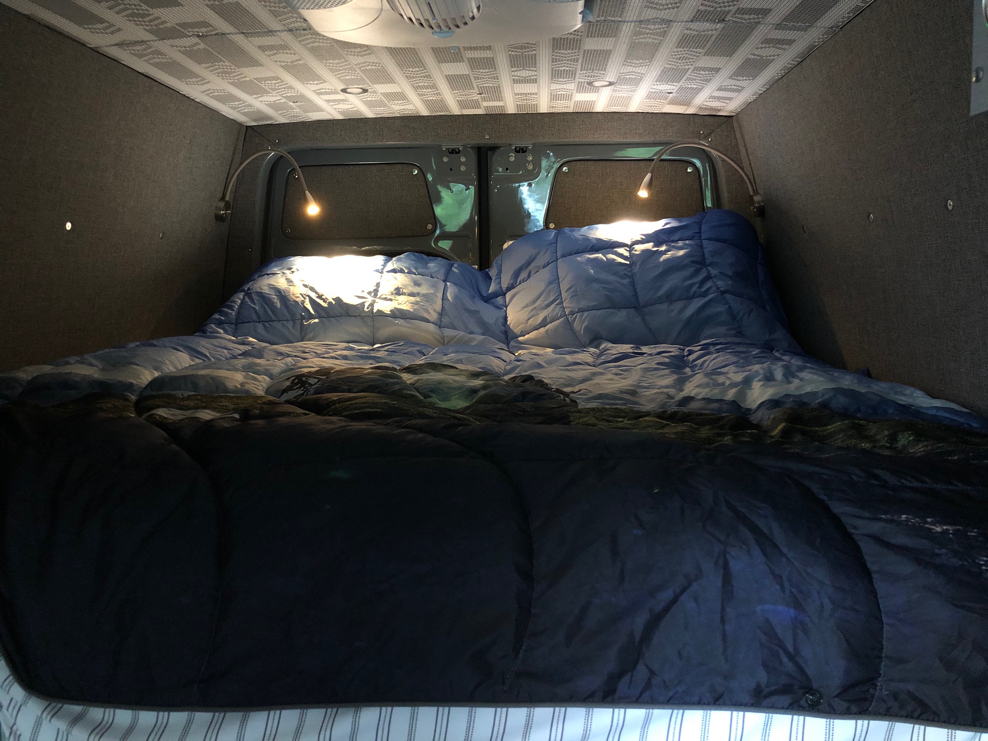 Cozy RV rental interior: A comfortable bed with blue comforters and two bright reading lights. Custom walls and ceiling.. Mercedes Sprinter 2022