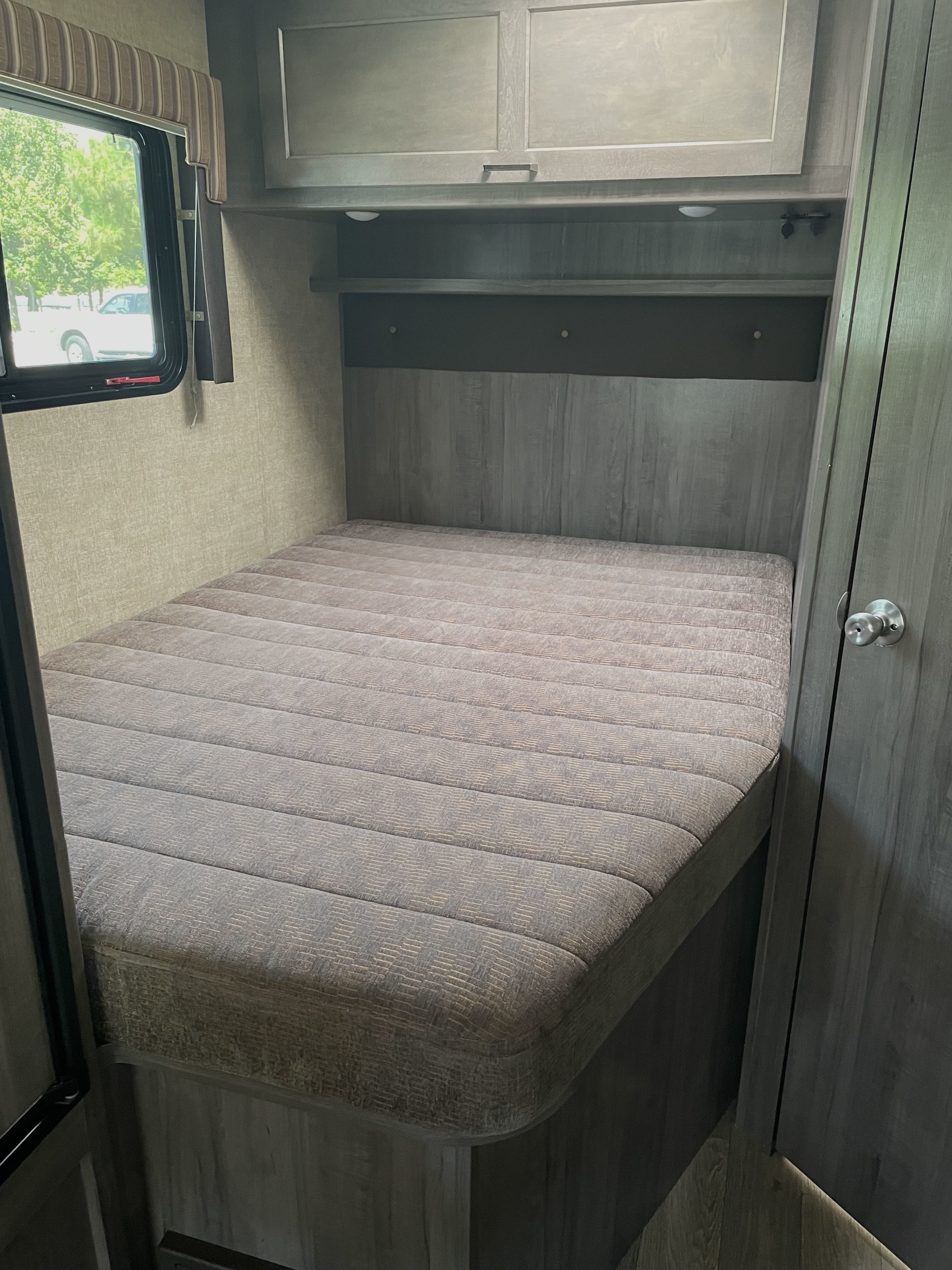 Inside an RV rental: a compact bedroom with a textured mattress, storage cabinets, and a window for natural light.. Winnebago Minnie Winnie 2019