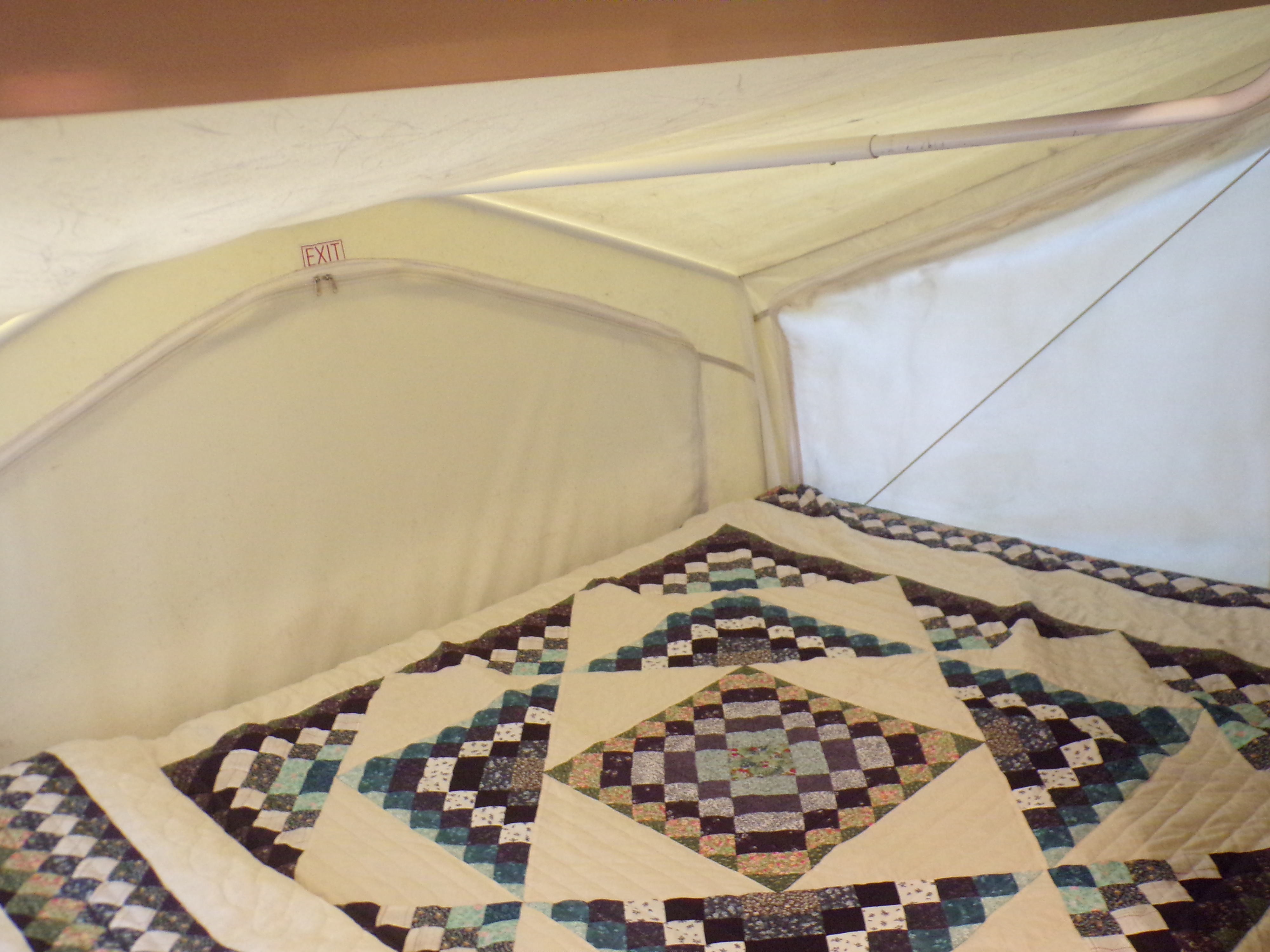 View inside an RV rental, showing a colorful quilted bed and an overhead EXIT sign in the pop-up ceiling.. Forest River Rockwood Roo 2011