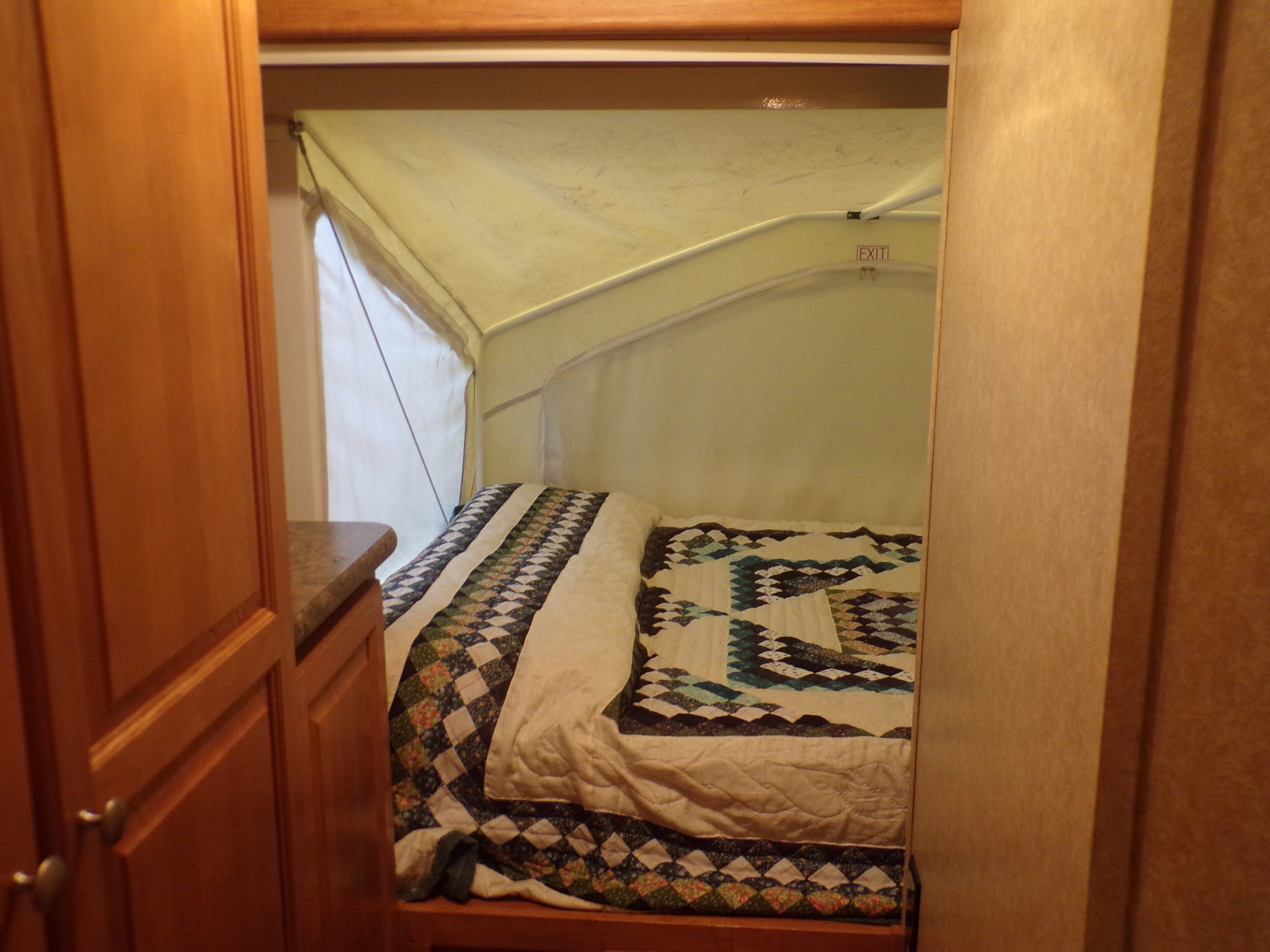 Inside an RV rental: a comfortable bed with colorful quilts, pop-up canvas walls, and an EXIT sign.. Forest River Rockwood Roo 2011