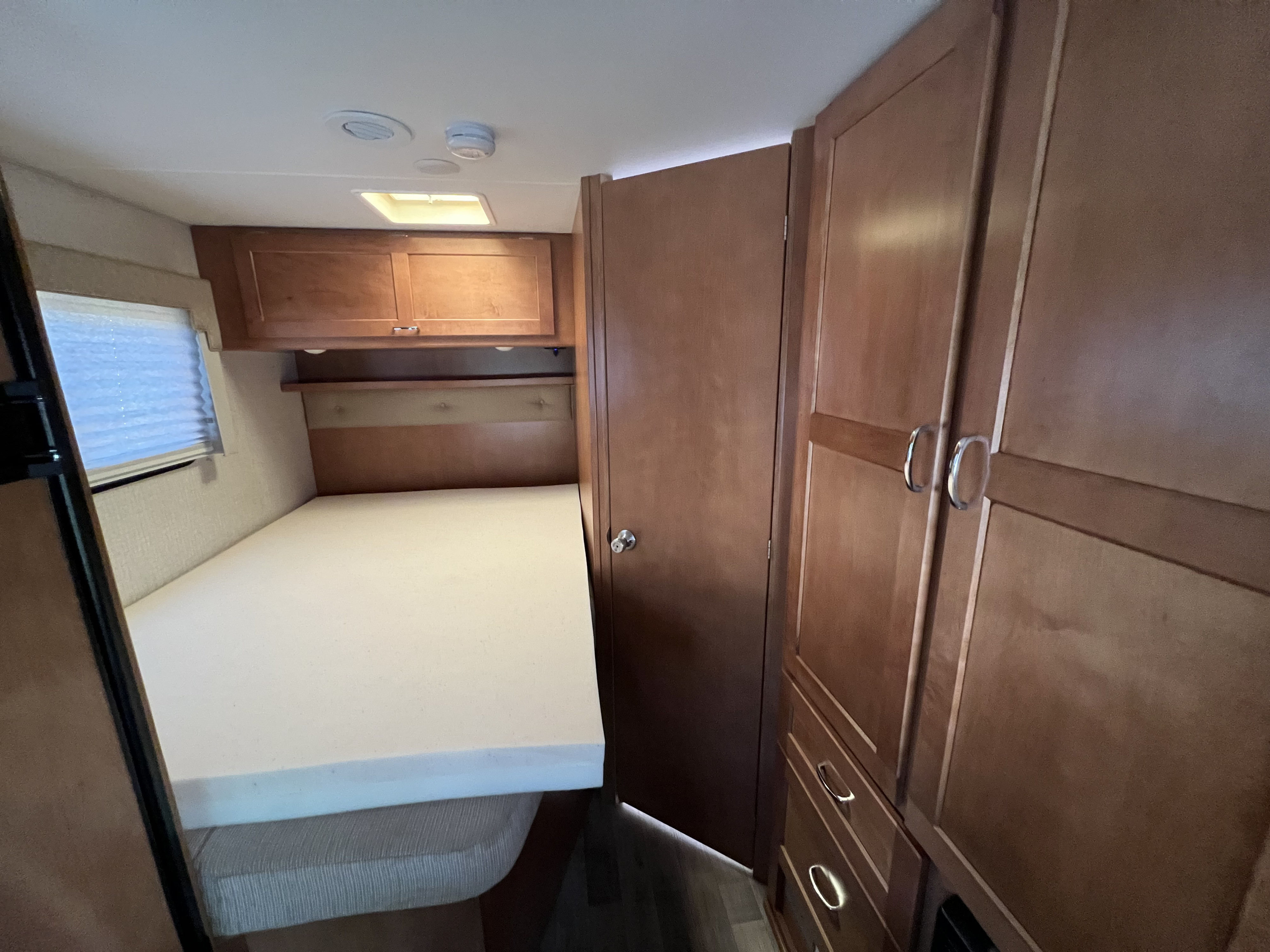 RV rental bedroom: A compact space with white mattress, wood cabinets, and window.. Winnebago Minnie Winnie 2018