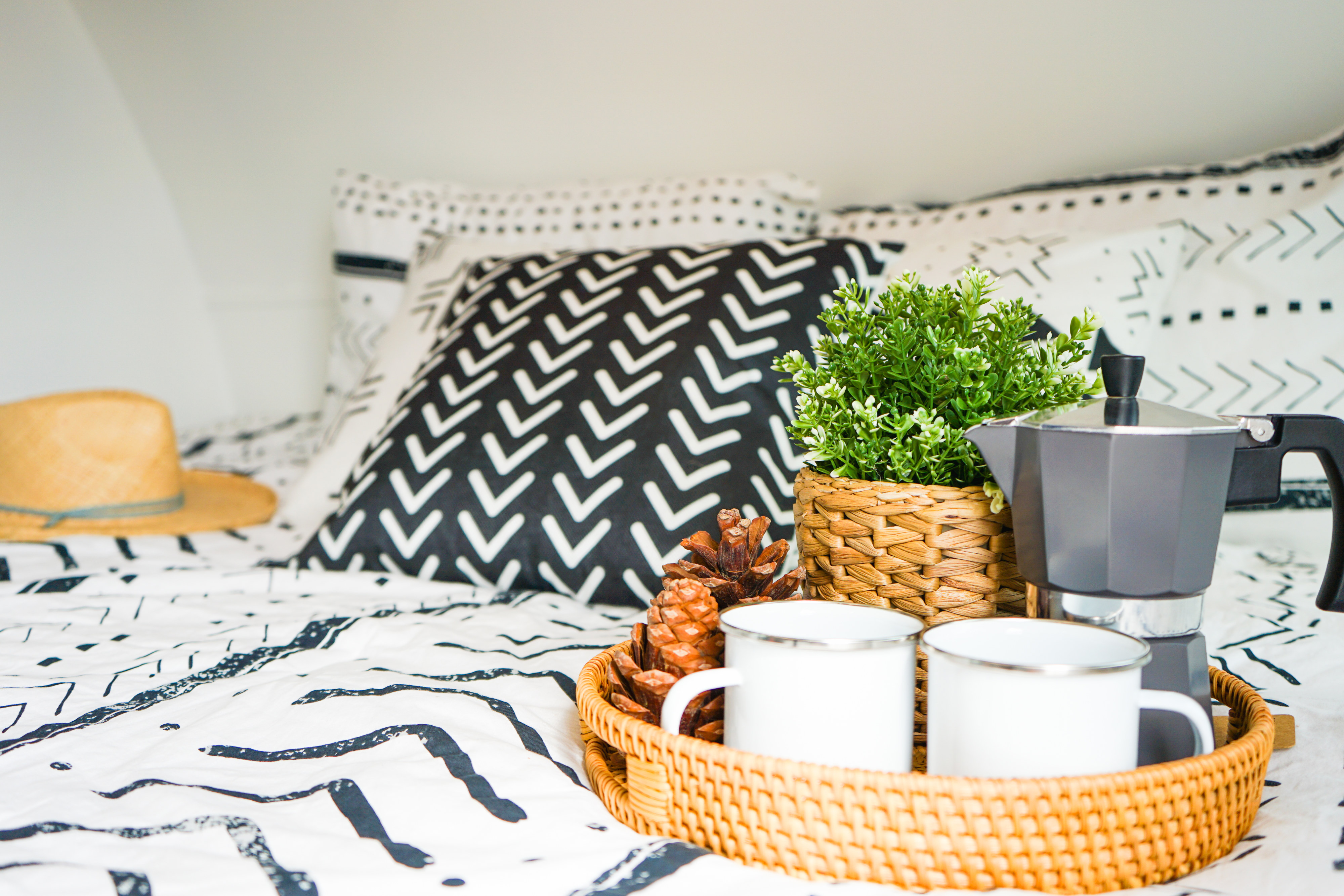 Enjoy a cozy RV rental morning. Bed with patterned bedding, Moka pot, mugs, and plant on a wicker tray.. Forest River Sonoma 1670BH 2020
