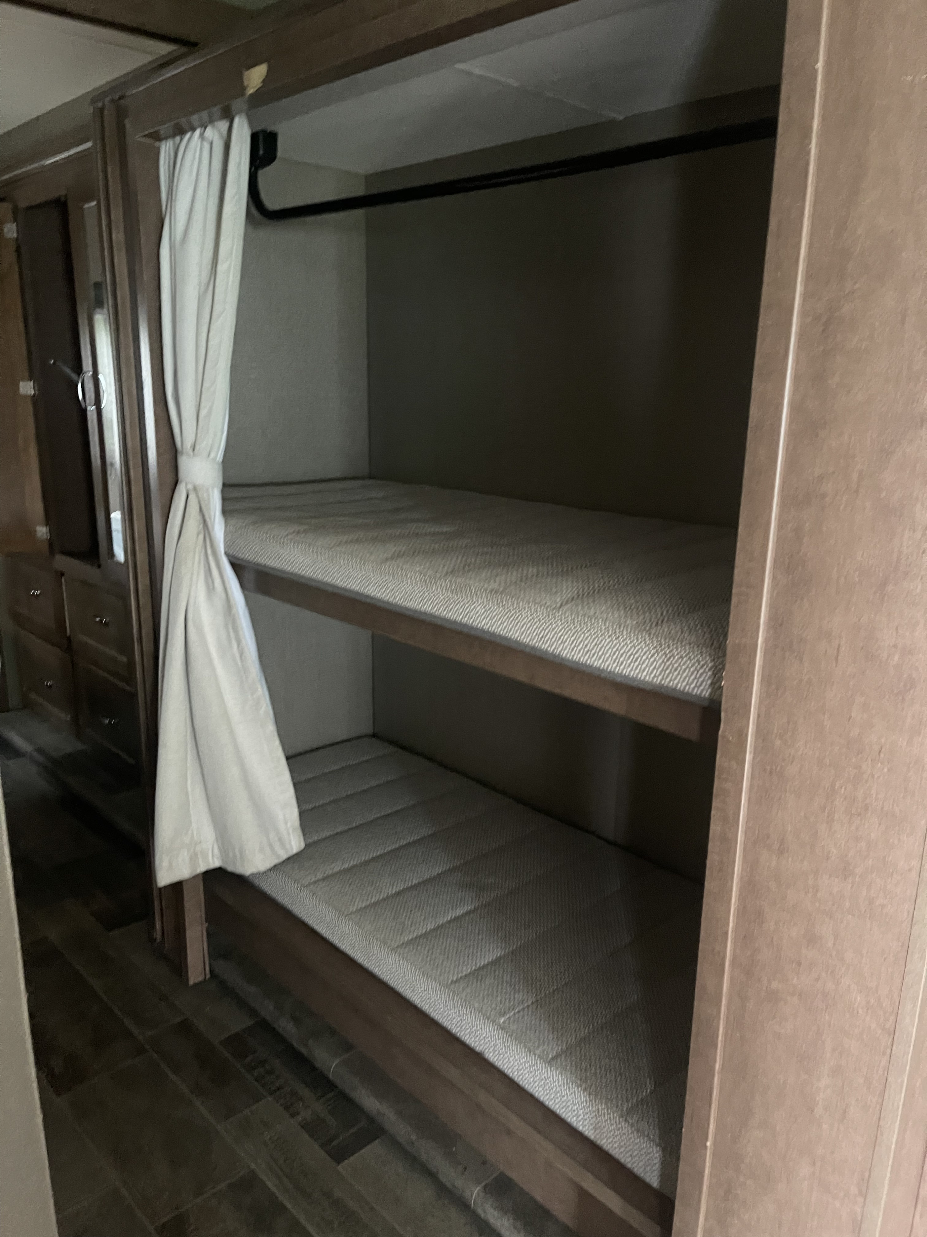 This RV rental shows bunk beds with light mattresses, a privacy curtain, and an adjacent storage unit.. Winnebago Intent 2019