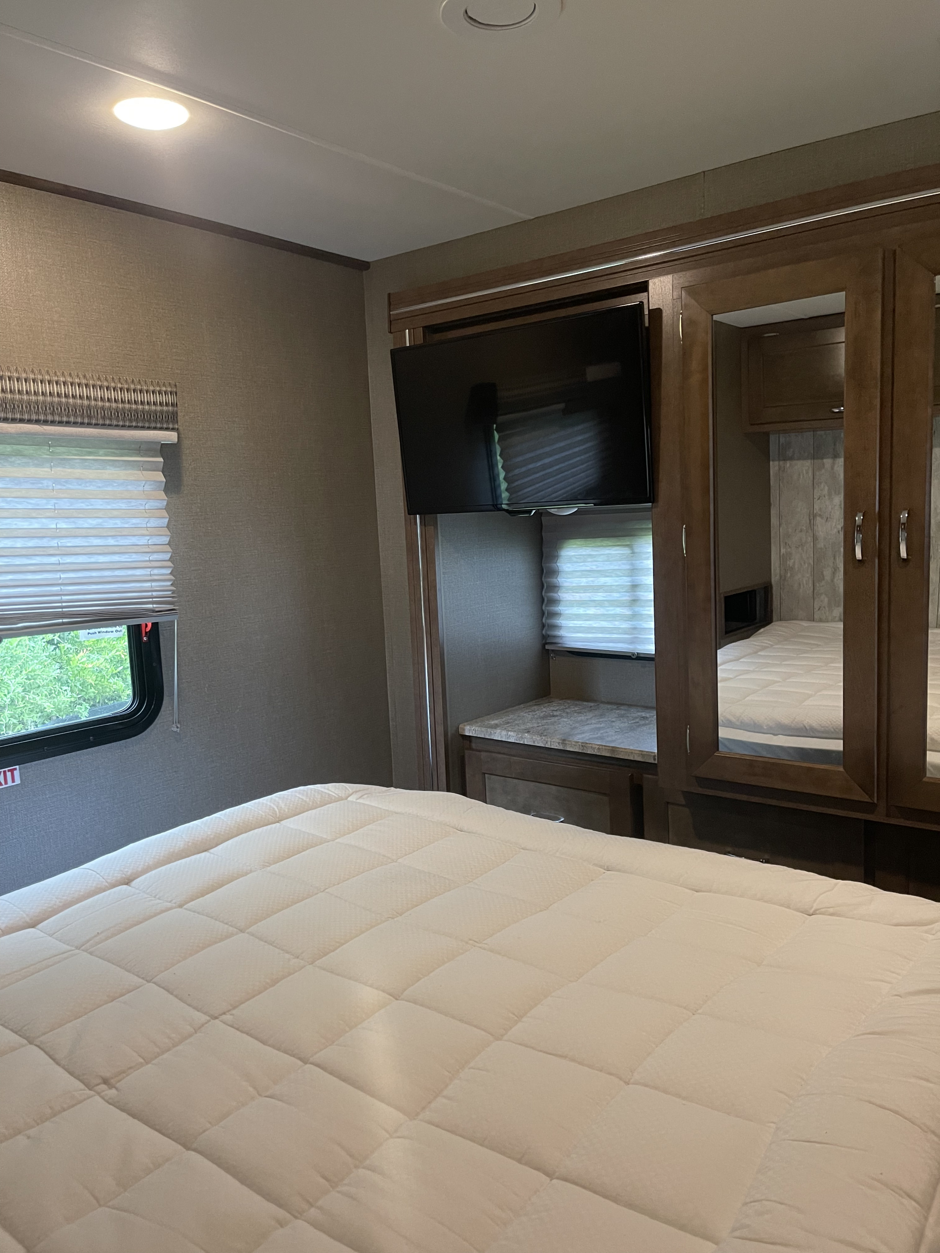 RV rental bedroom featuring a quilted bed, wall-mounted TV, storage, and window with blinds. A compact, functional travel space.. Winnebago Intent 2019