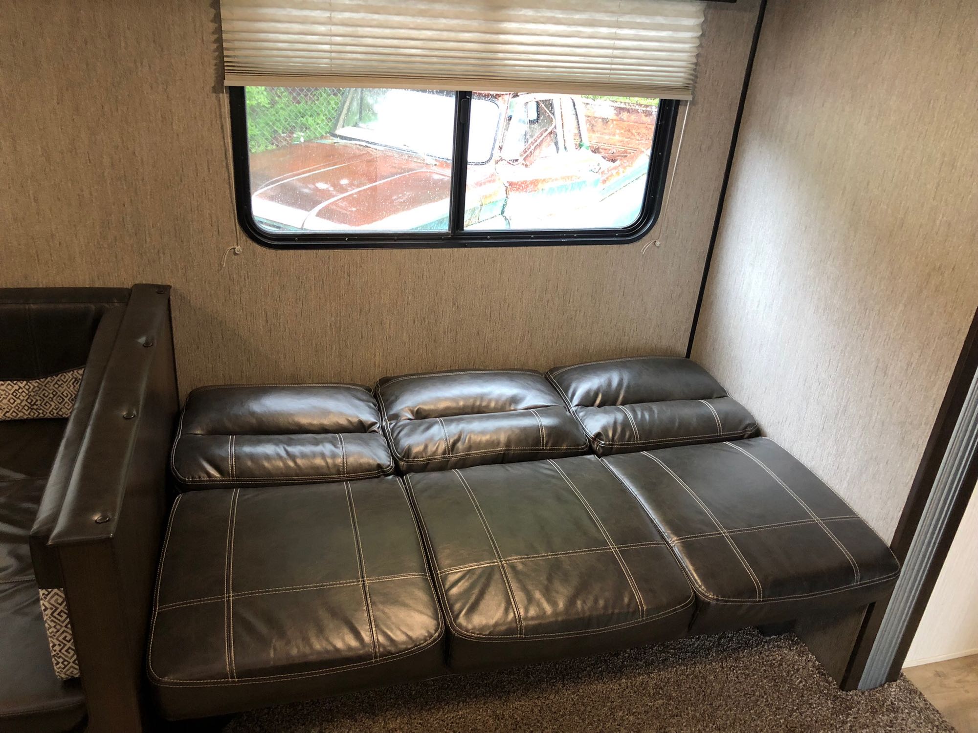 Comfortable RV rental interior with faux leather sofa/bed & window view of an old truck.. Heartland Prowler 2020