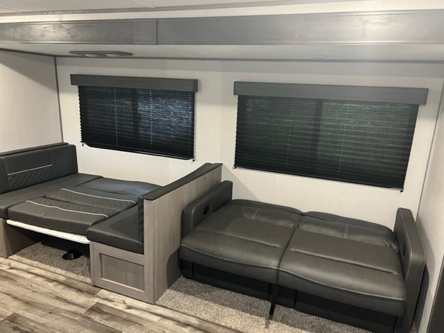 RV rental interior showing a dinette converted to a bed and a pull-out sofa bed, with dark window blinds.. Dutchmen Coleman Lantern 2022