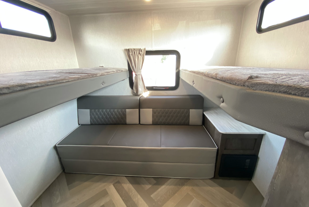 Modern RV rental interior featuring cozy bunk beds, a convertible sofa, and a bright window. Perfect for family trips.. Forest River Wildwood X-Lite 2022