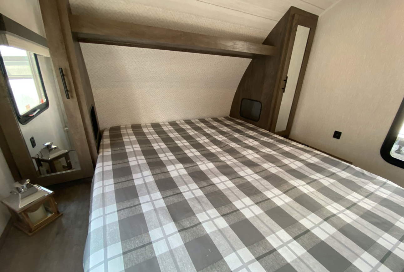 Inside an RV rental: a compact bedroom with plaid bedding, built-in storage, and mirrored doors.. Forest River Wildwood X-Lite 2022