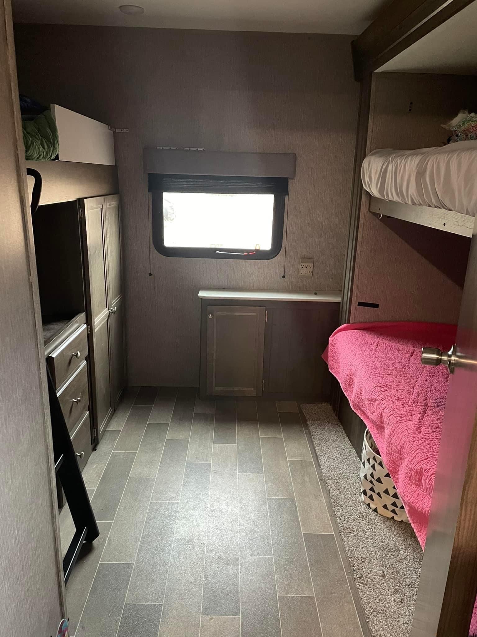 RV rental bedroom with bunk beds, storage cabinets, and a bright window, offering a cozy interior view.. Dutchmen Coleman Lantern 2020