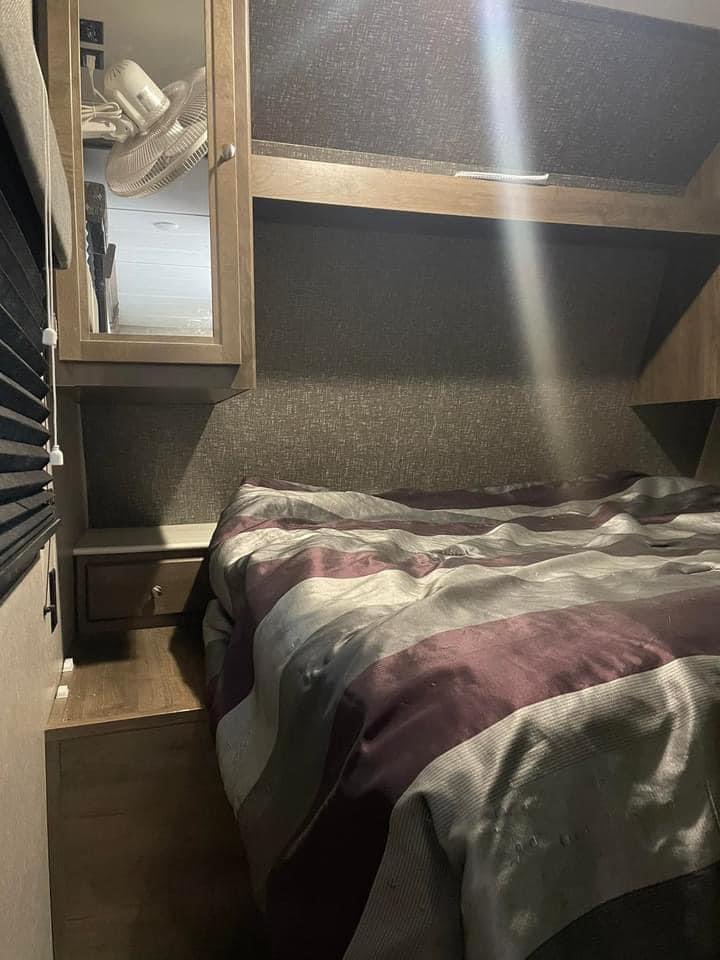 Inside an RV rental: compact bedroom featuring a striped bed, built-in nightstand, and mirrored storage cabinet.. Dutchmen Coleman Lantern 2020