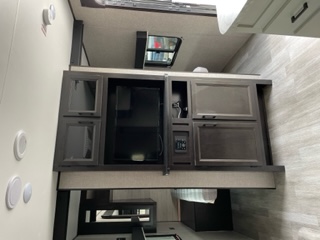 RV rental interior: A dark wood entertainment center with a TV, storage cabinets, and control panel is shown.. Jayco Jay Flight SLX 8 2023