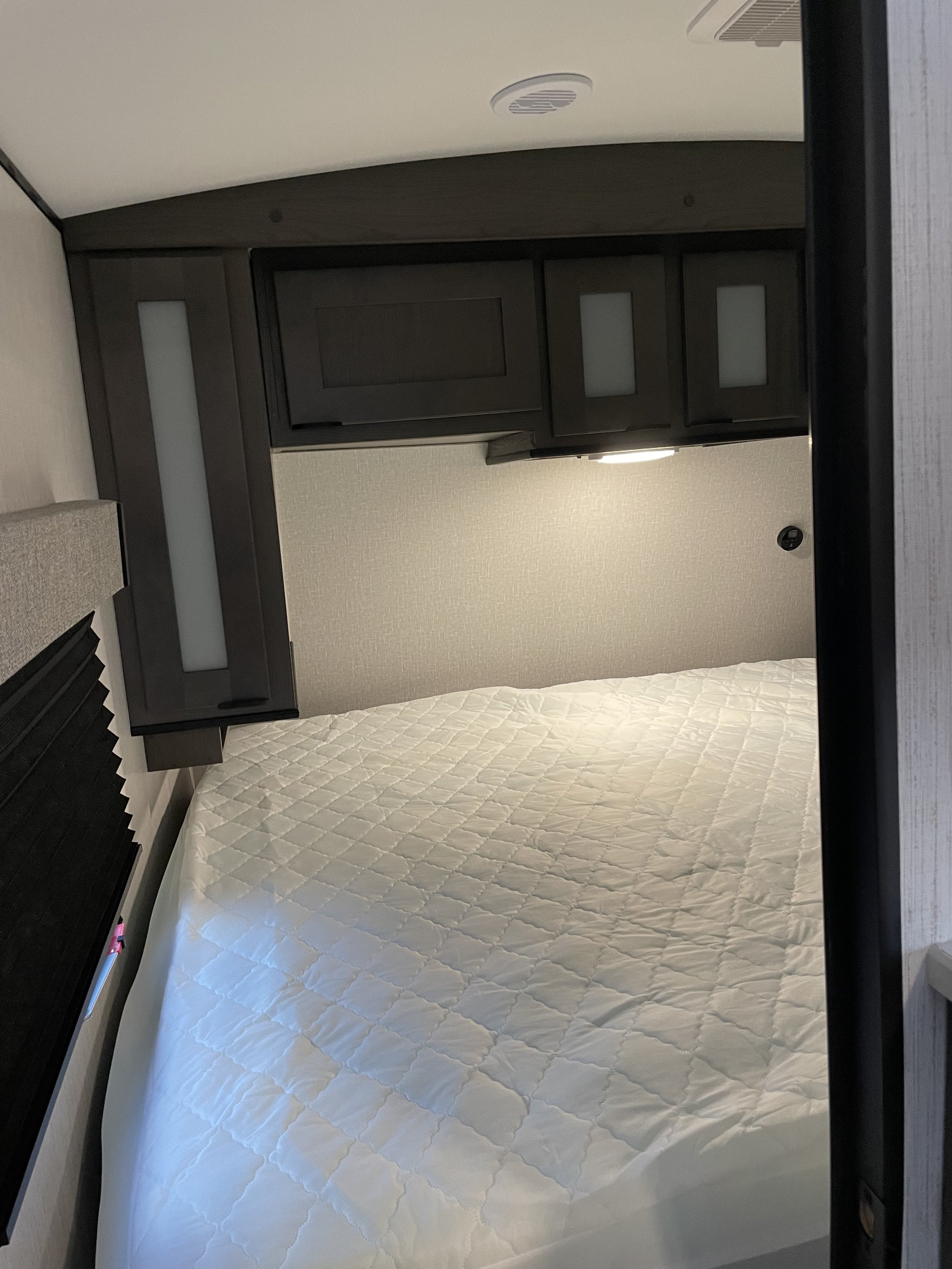Comfortable RV rental bedroom featuring overhead storage, a quilted bed, and bedside lighting, ideal for cozy travel.. Heartland Mpg 2022