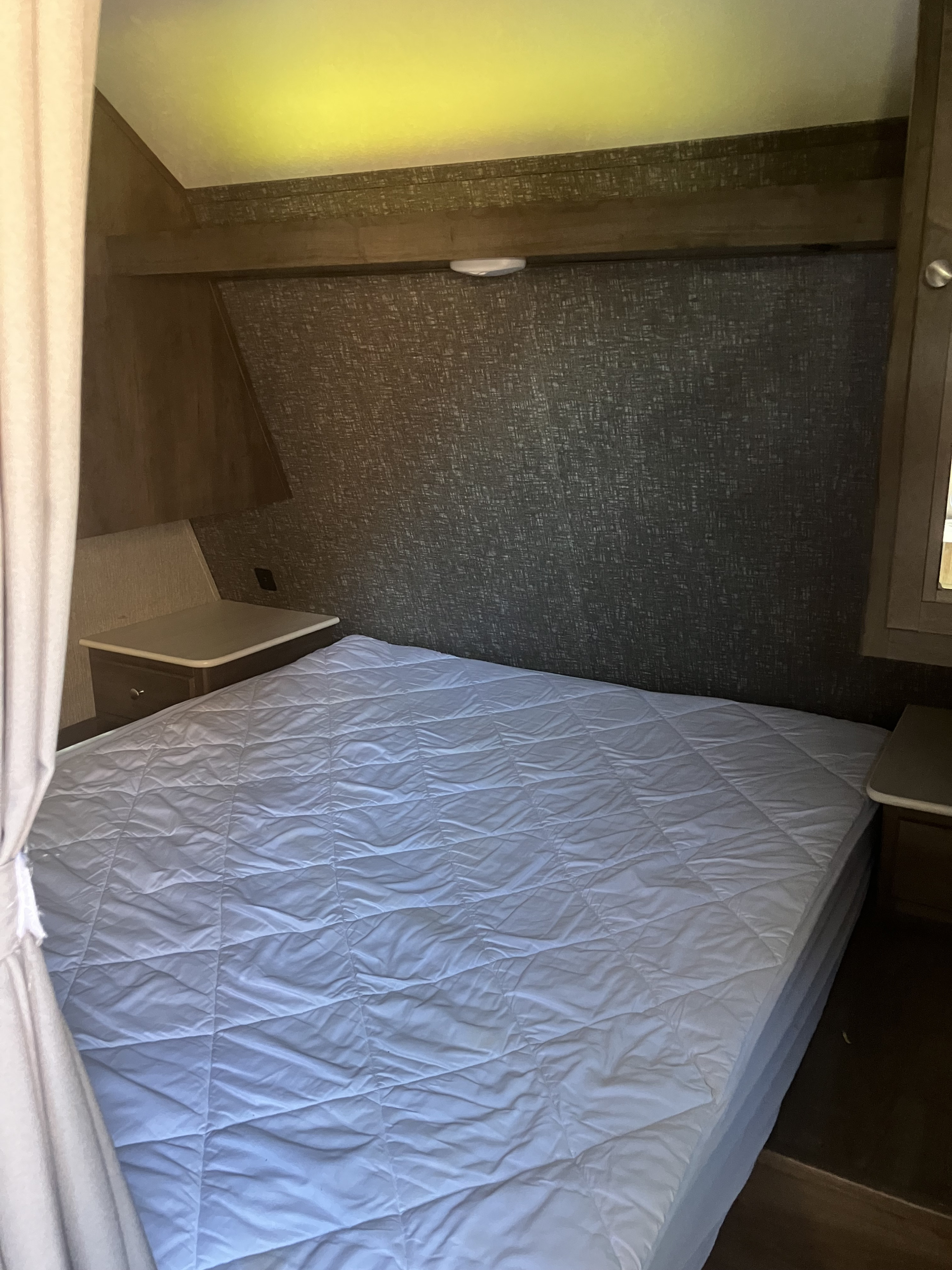 Cozy RV rental bedroom featuring a clean, white quilted bed, built-in nightstands, and textured walls for comfortable travel.. Dutchmen Coleman Lantern 2019