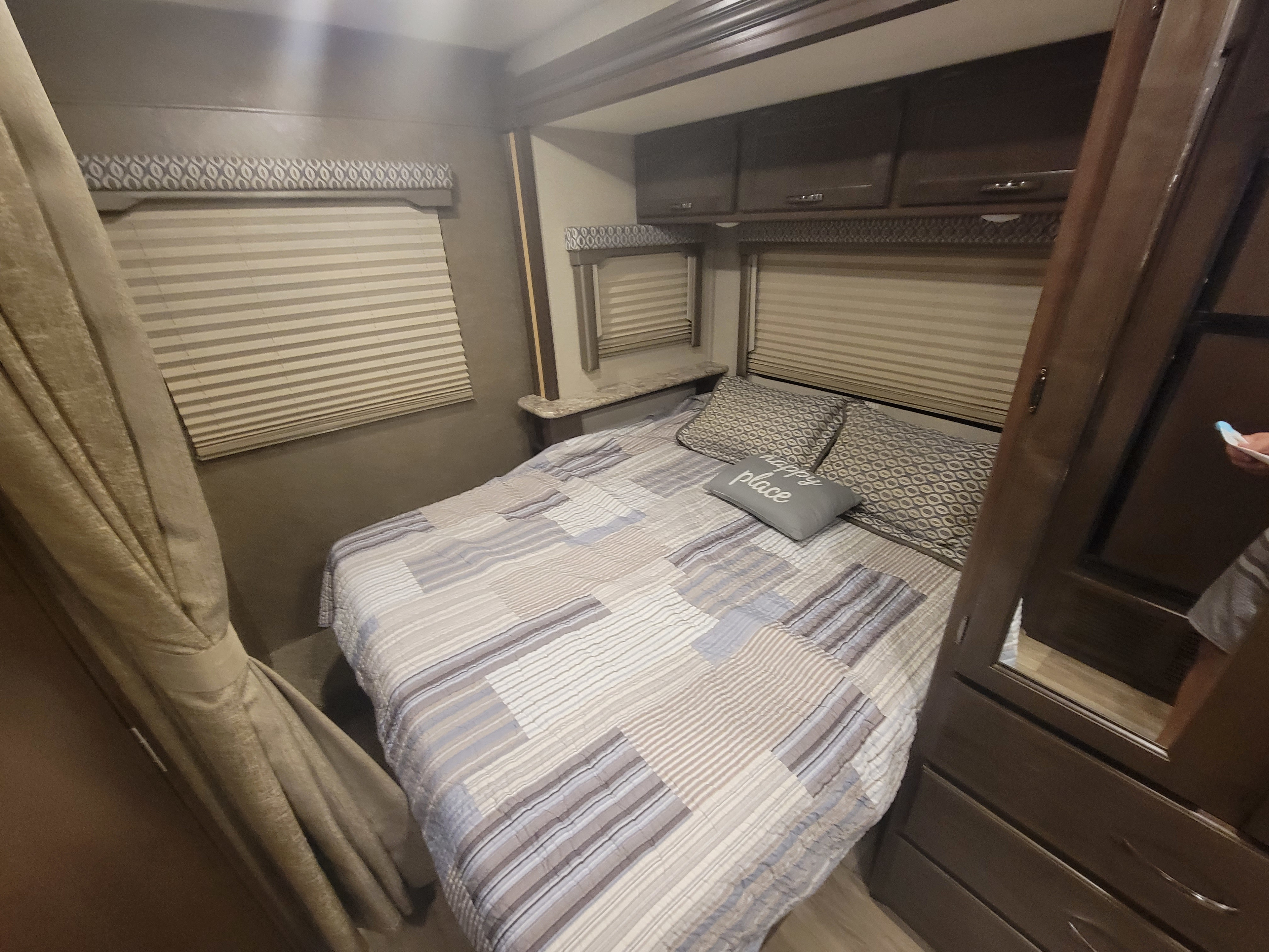 RV rental bedroom: Cozy interior with bed, window blinds, patterned valances, and overhead cabinets.. Thor Freedom Elite 2020