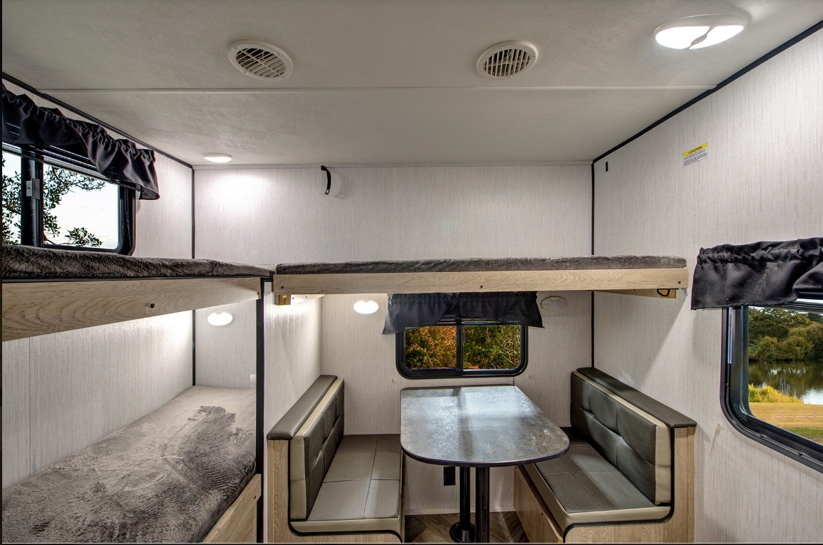 View inside an RV rental showing light wood bunk beds, a gray upholstered dinette, and bright windows.. Heartland Prowler 2022