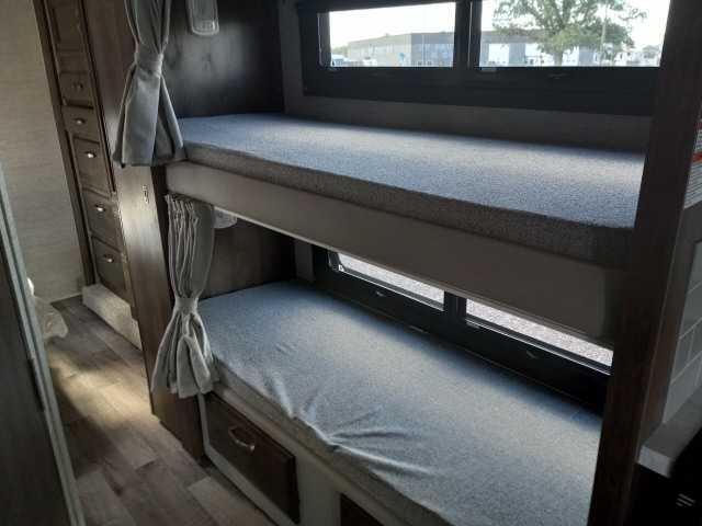 RV rental interior: Stacked bunk beds with gray mattresses and privacy curtains are visible, along with storage.. Jayco Greyhawk 2021